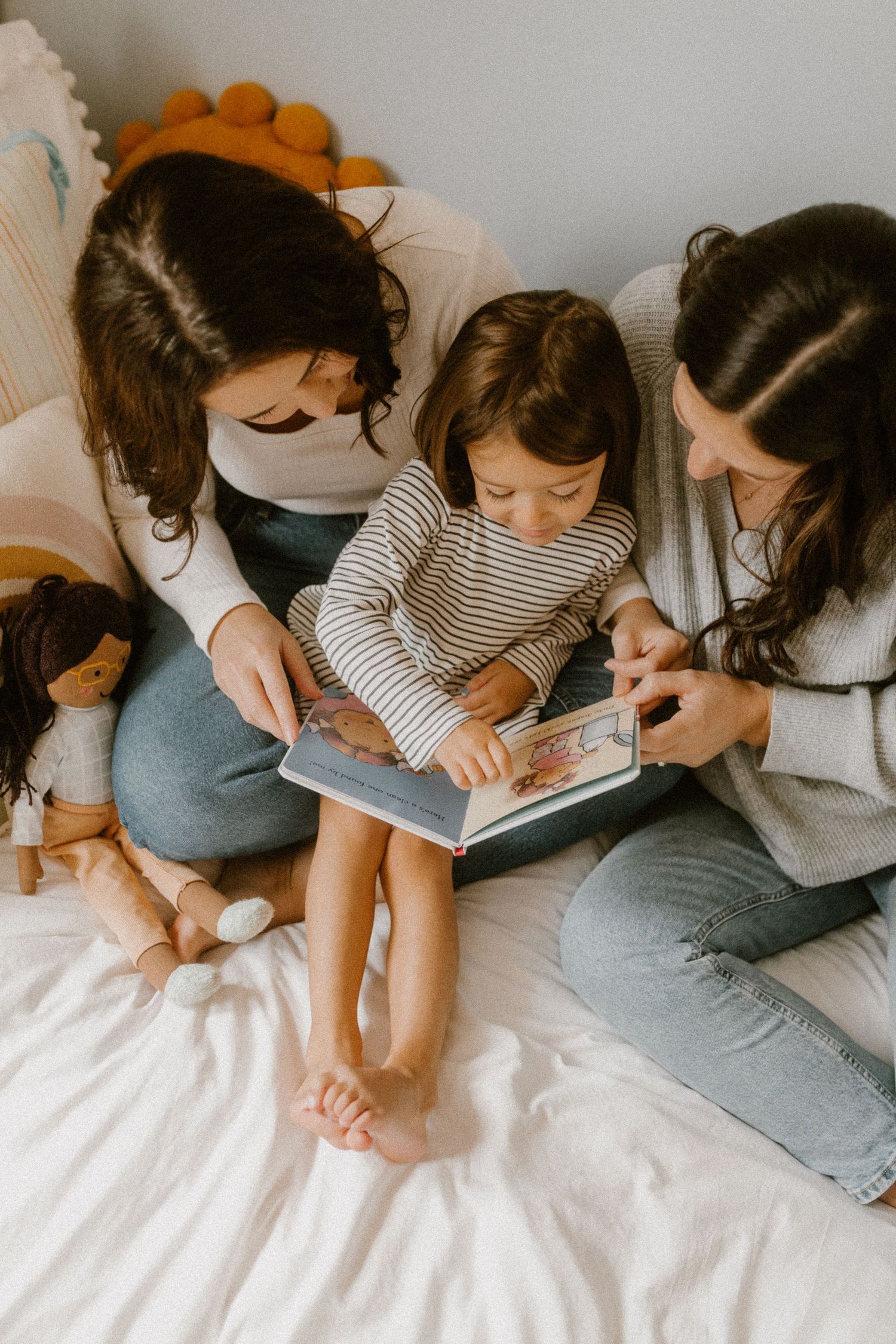 Family reading time together on a cozy white bed with a doll toy nearby.