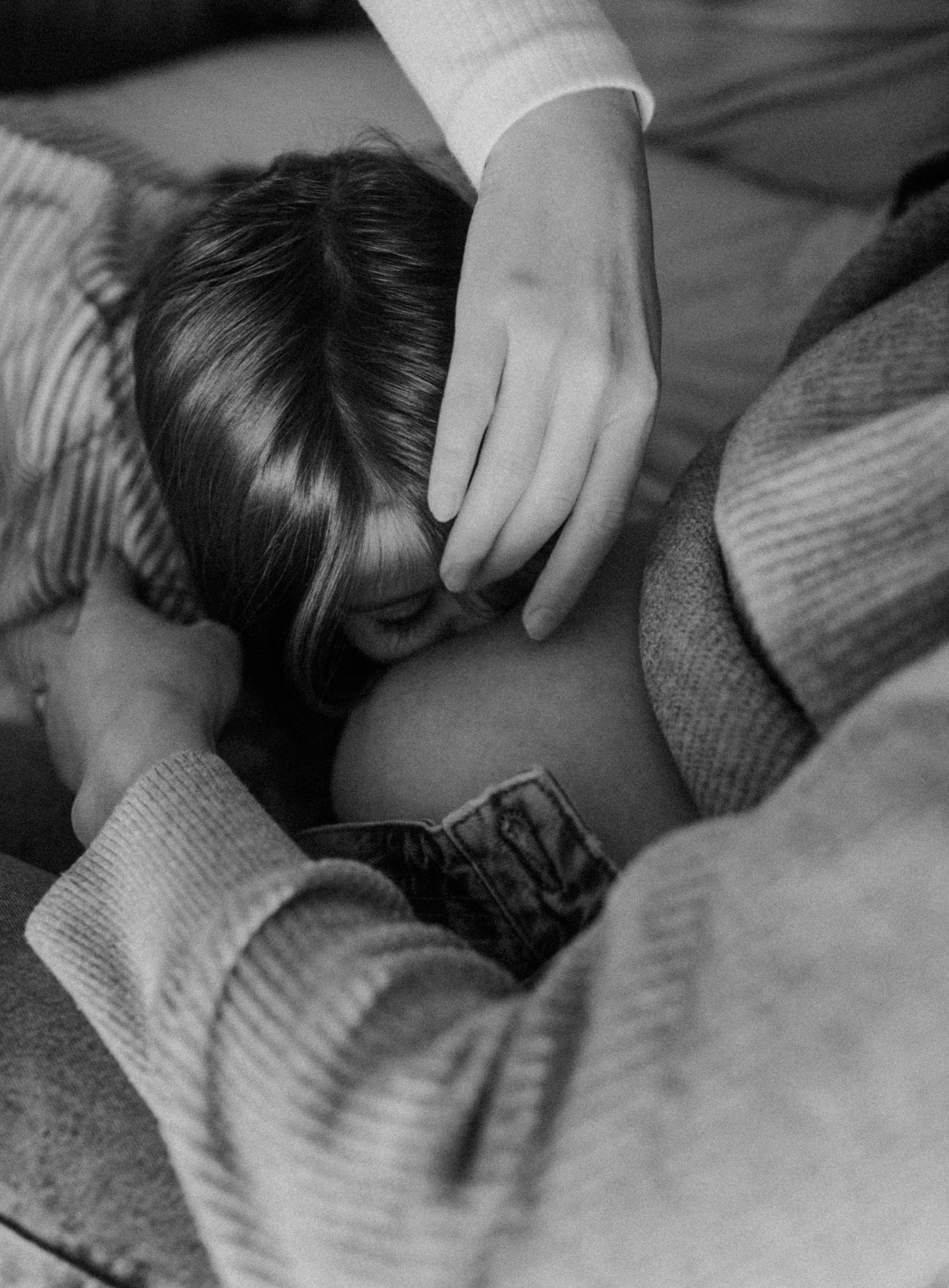 Close-up black and white image of young girl kissing her mom's pregnant belly as her wife touches their daughter.