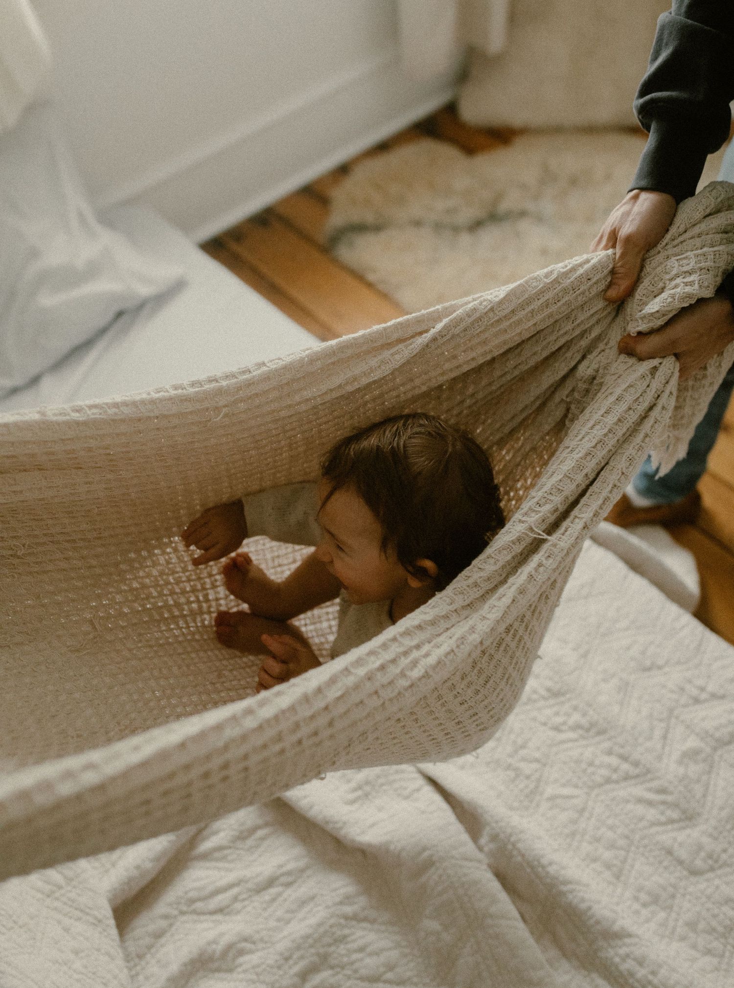 A small child nestled in a cozy white hammock indoors while someone adjusts the fabric.