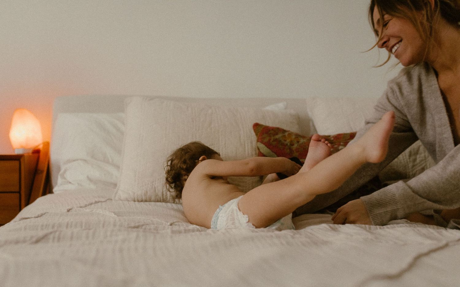 Cozy morning bedroom scene with warm lighting from bedside lamp as someone relaxes on white bedding during evening time.