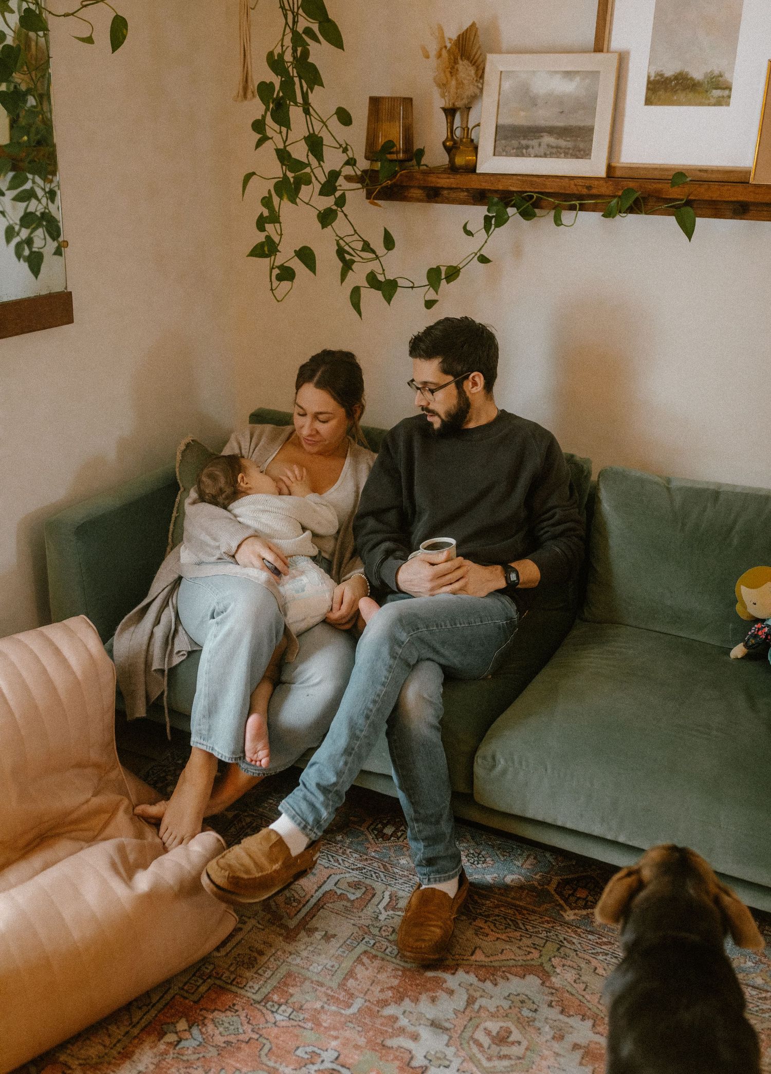 A couple relaxes on a green couch with trailing plants and vintage decor in a warm-toned living room.