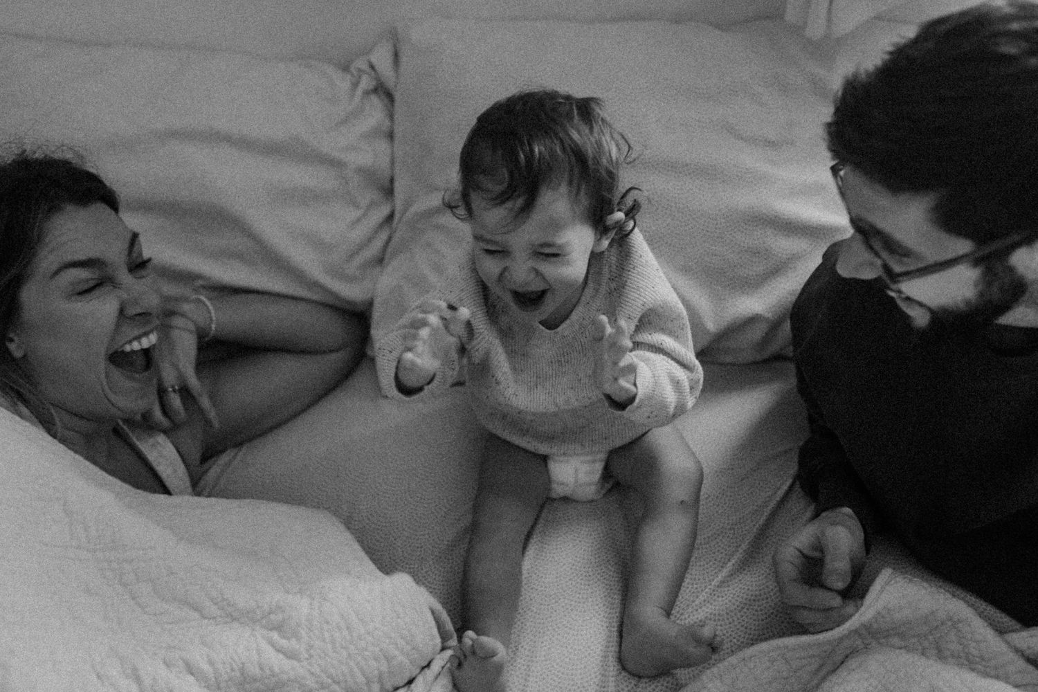 Black and white candid photo showing animated family interaction on bedding.