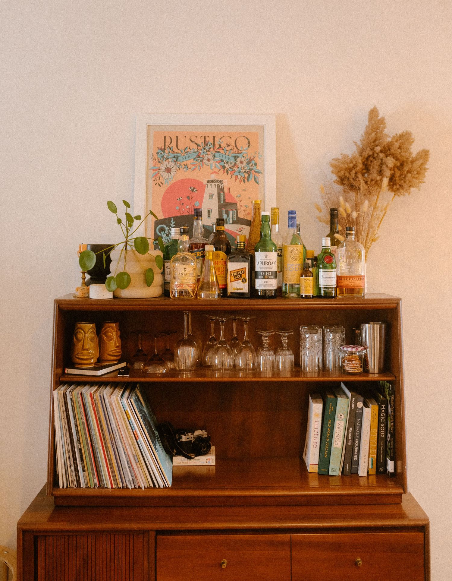 A vintage-style bar cart with liquor bottles, glassware, vinyl records, and rustic decor.