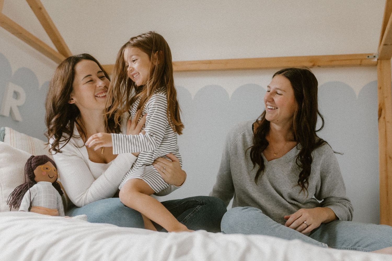 Family with two moms sharing a joyful moment while relaxing together on a cozy bed.
