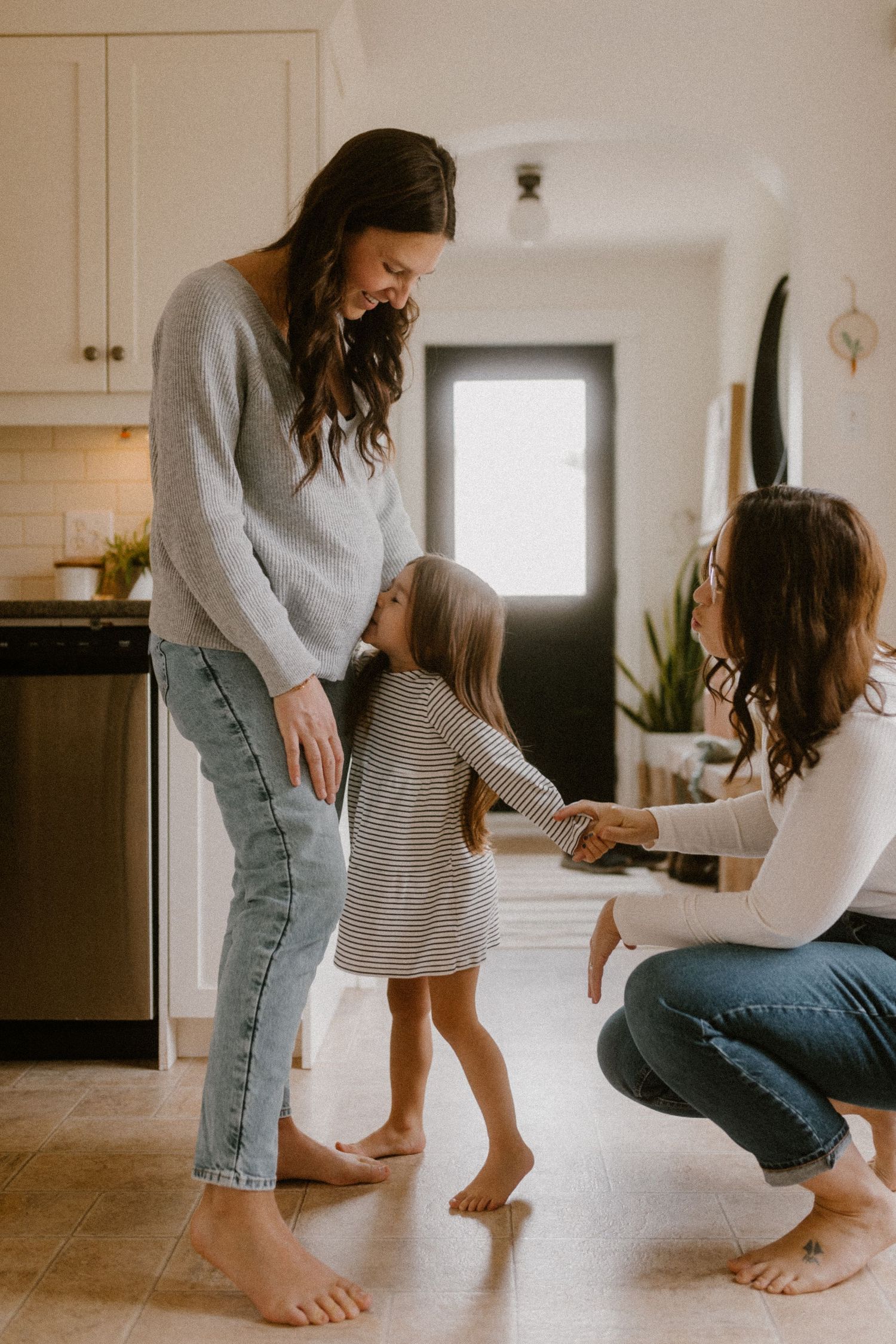Three people interacting playfully in modern kitchen with white cabinets and wood floors.