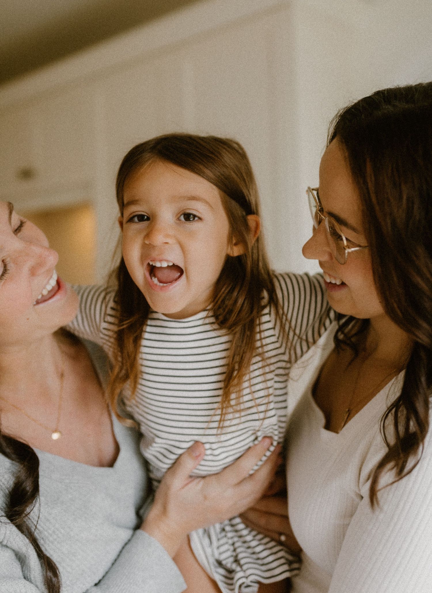 Candid moment of laughter and joy captured in natural light between two moms and daughter.