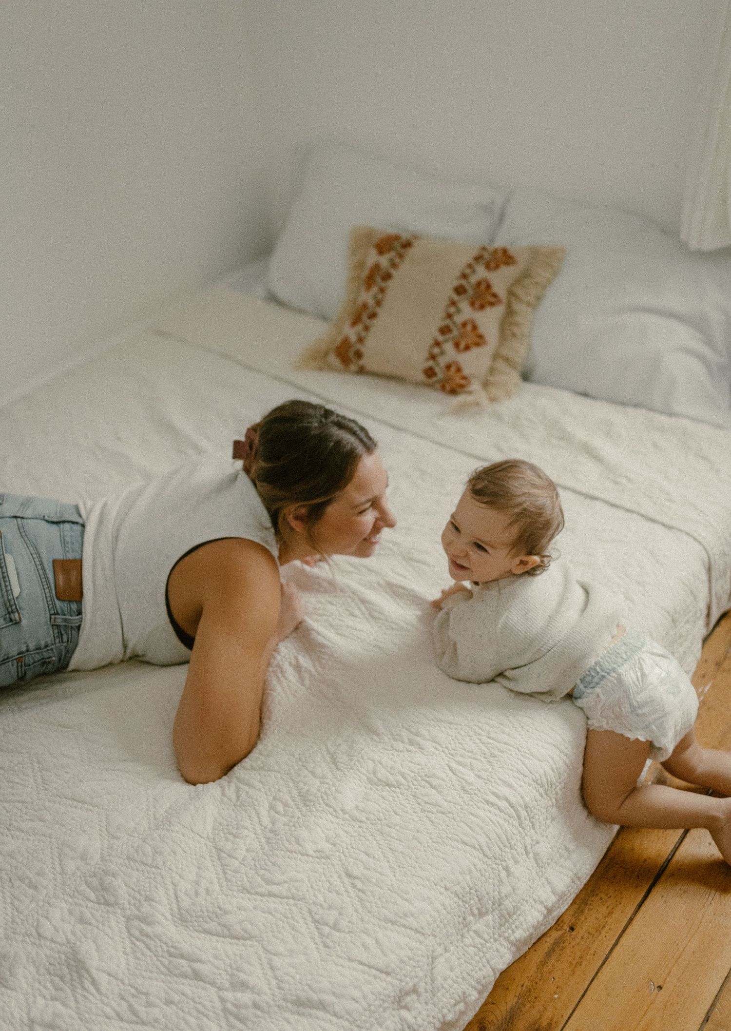 Intimate family moment captured on white bedding with natural light streaming through window.
