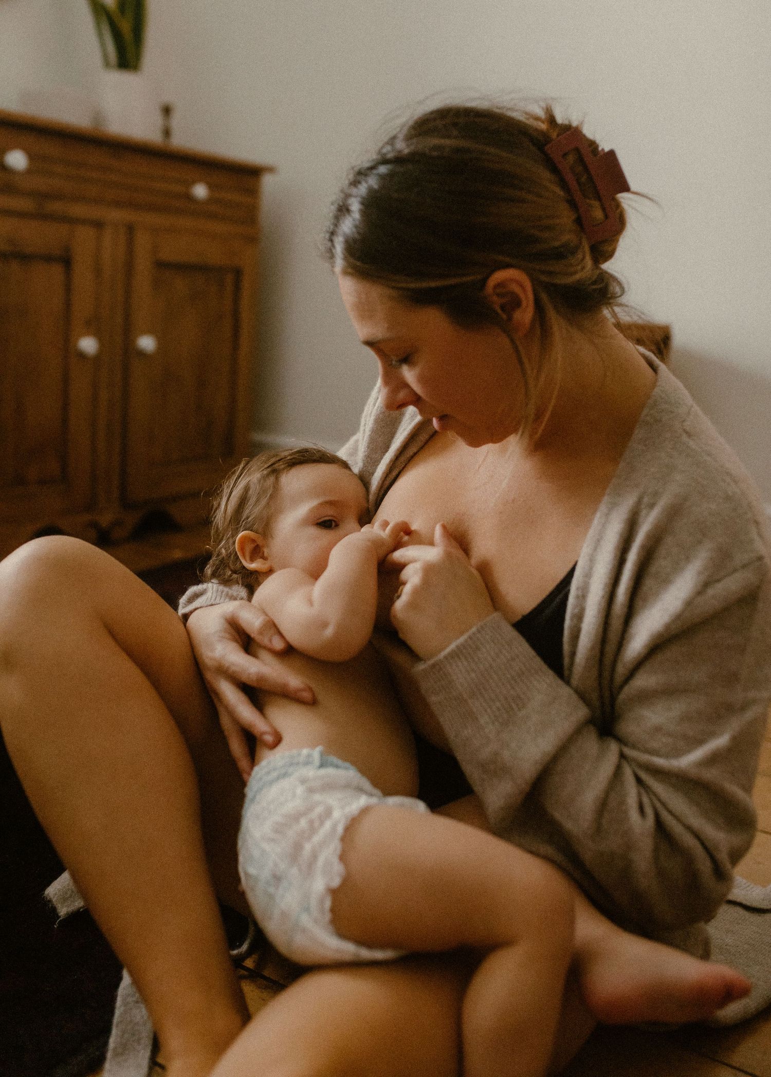 A tender bonding moment of breastfeeding in warm lighting shows a parent in a gray sweater nurturing their baby.