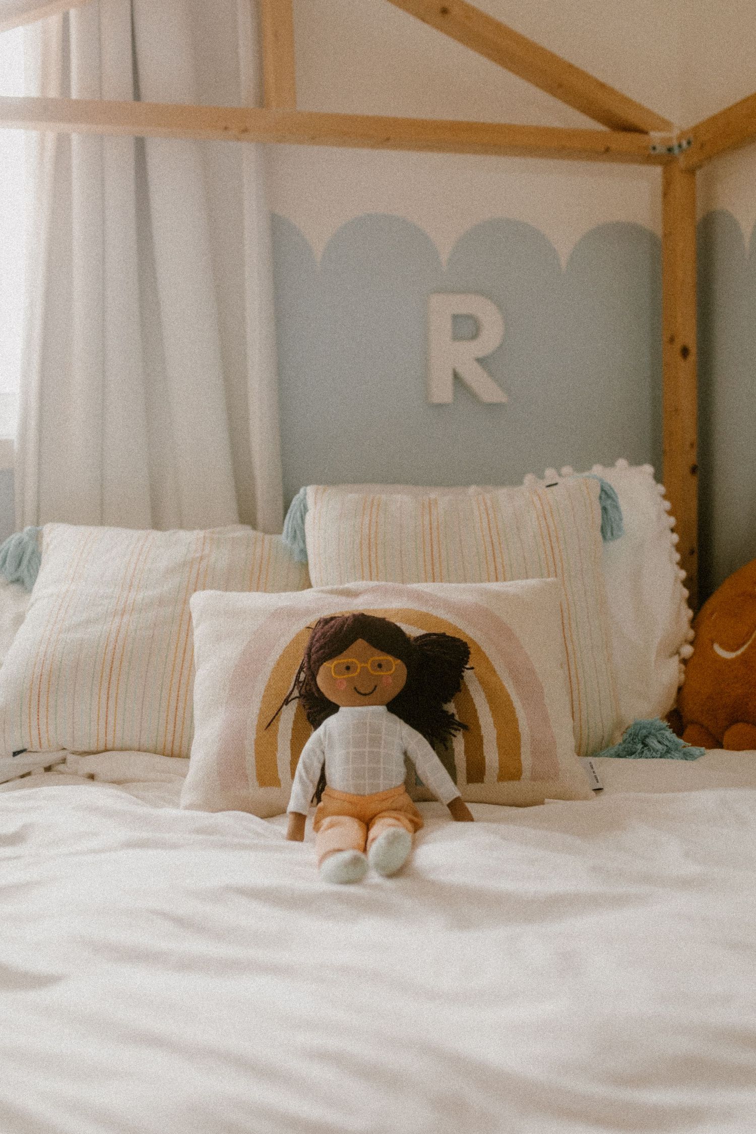 A cozy bed with white linens, wooden canopy frame, and decorative plush doll against blue scalloped wall.