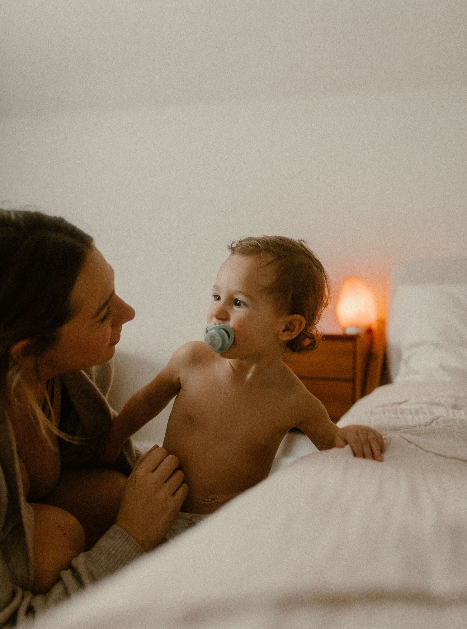 A tender bedtime moment between parent and child illuminated by warm lamplight in a cozy bedroom setting.