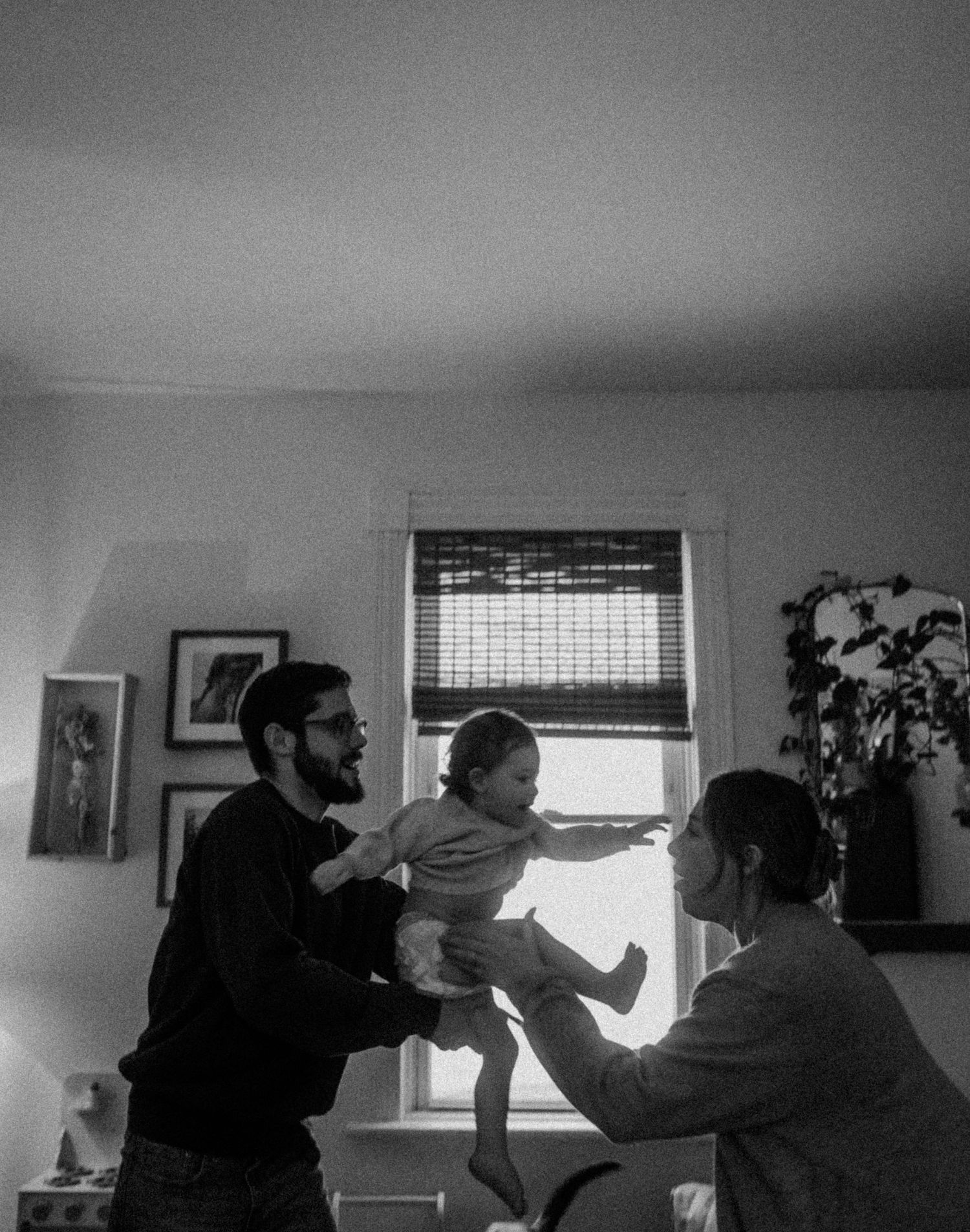 A black and white photograph capturing a joyful family moment indoors.