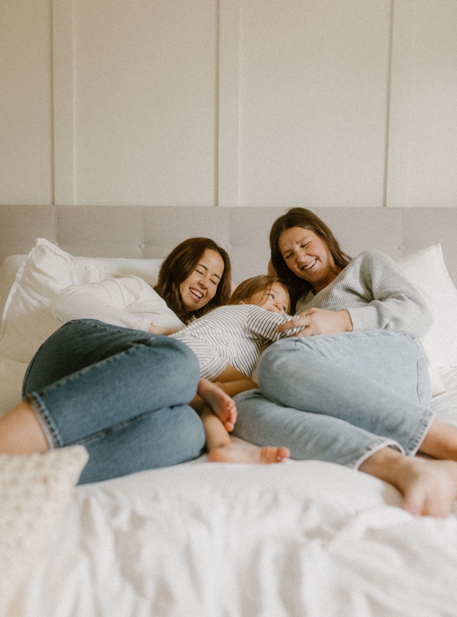 Family members relaxing together on a white bed wearing jeans and casual clothes.
