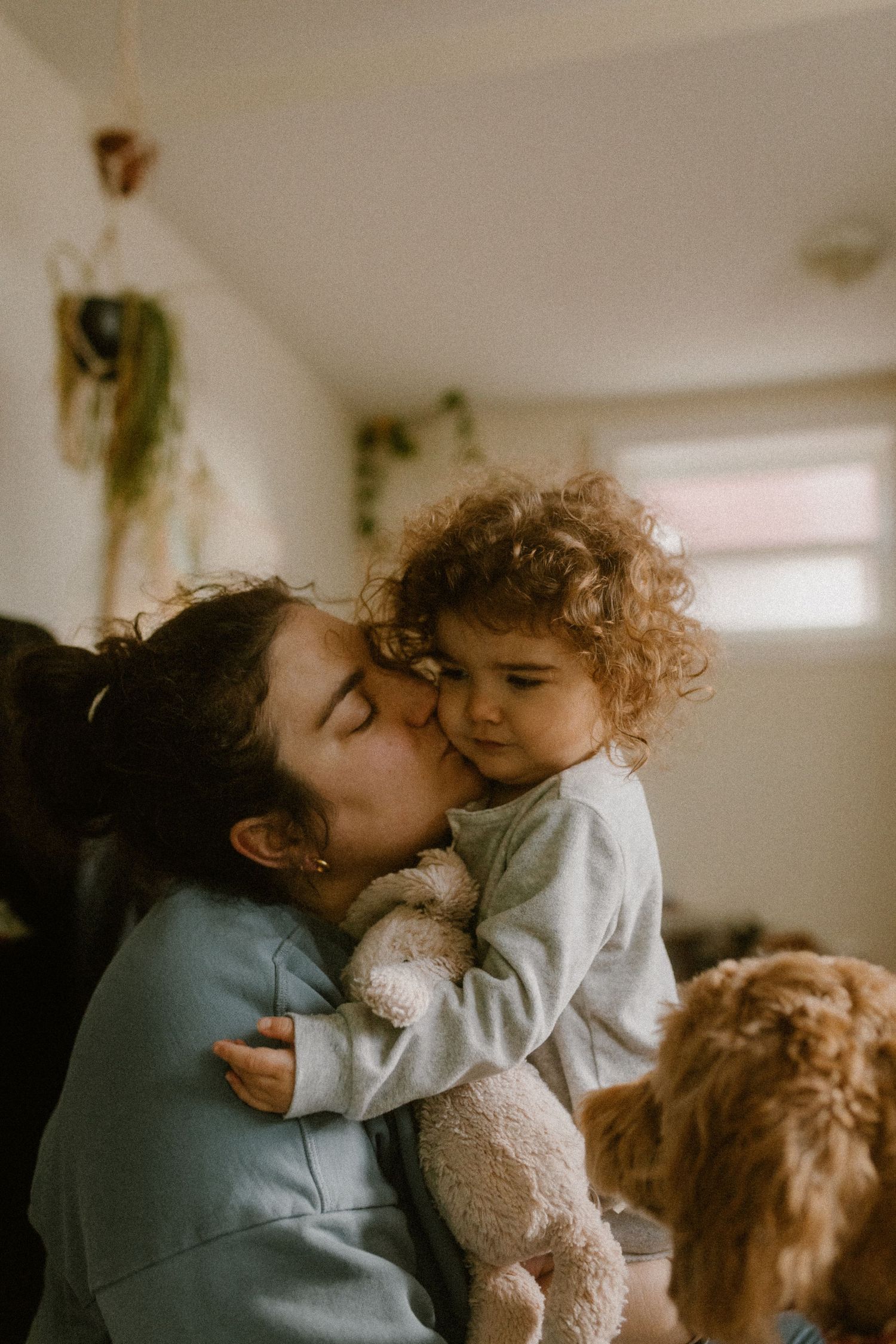 An intimate family moment at home showcasing a tender embrace while holding a stuffed animal while dog is watching.