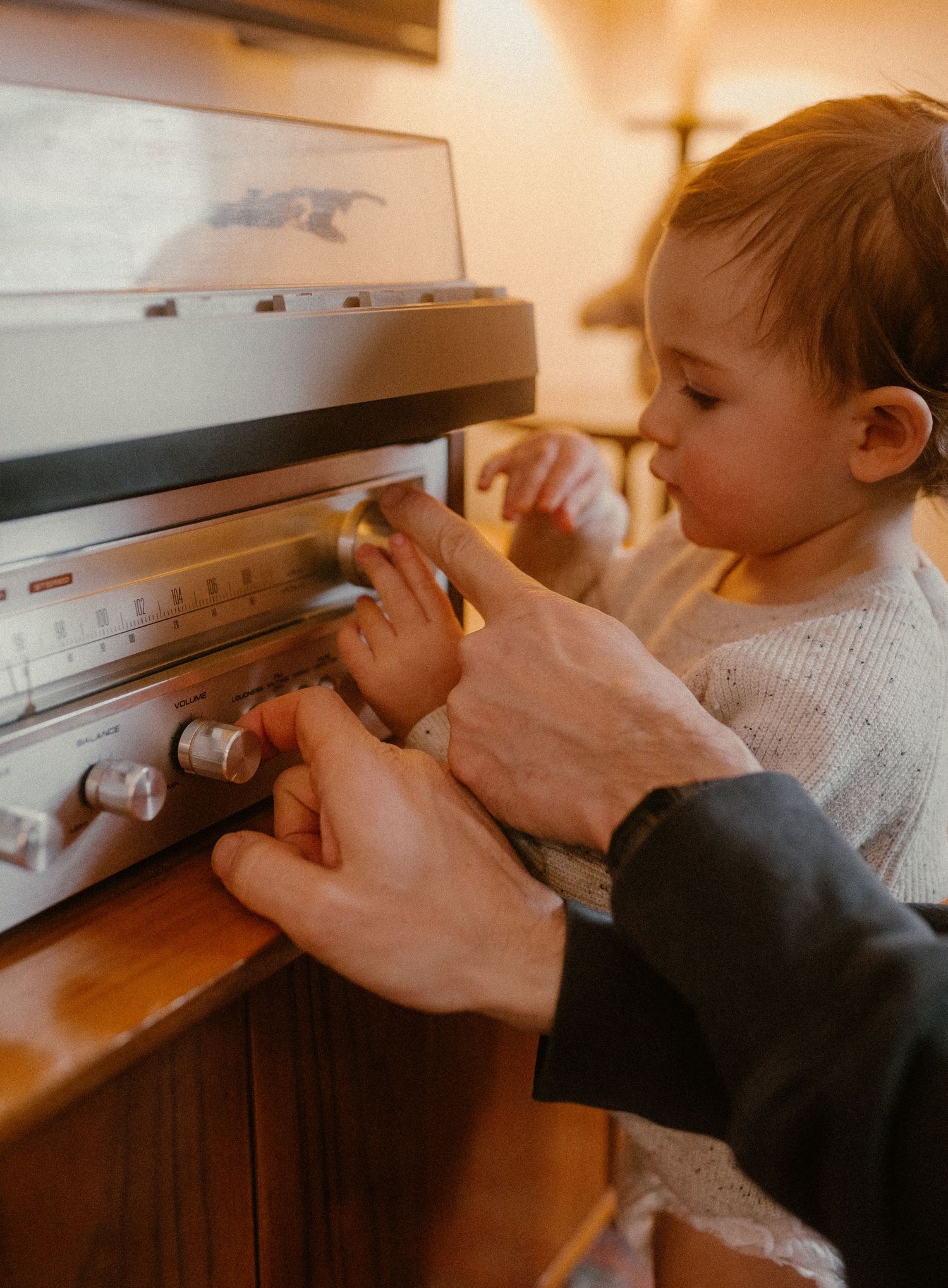 A child's hands reach up to explore a vintage stereo system with assistance from an adult.