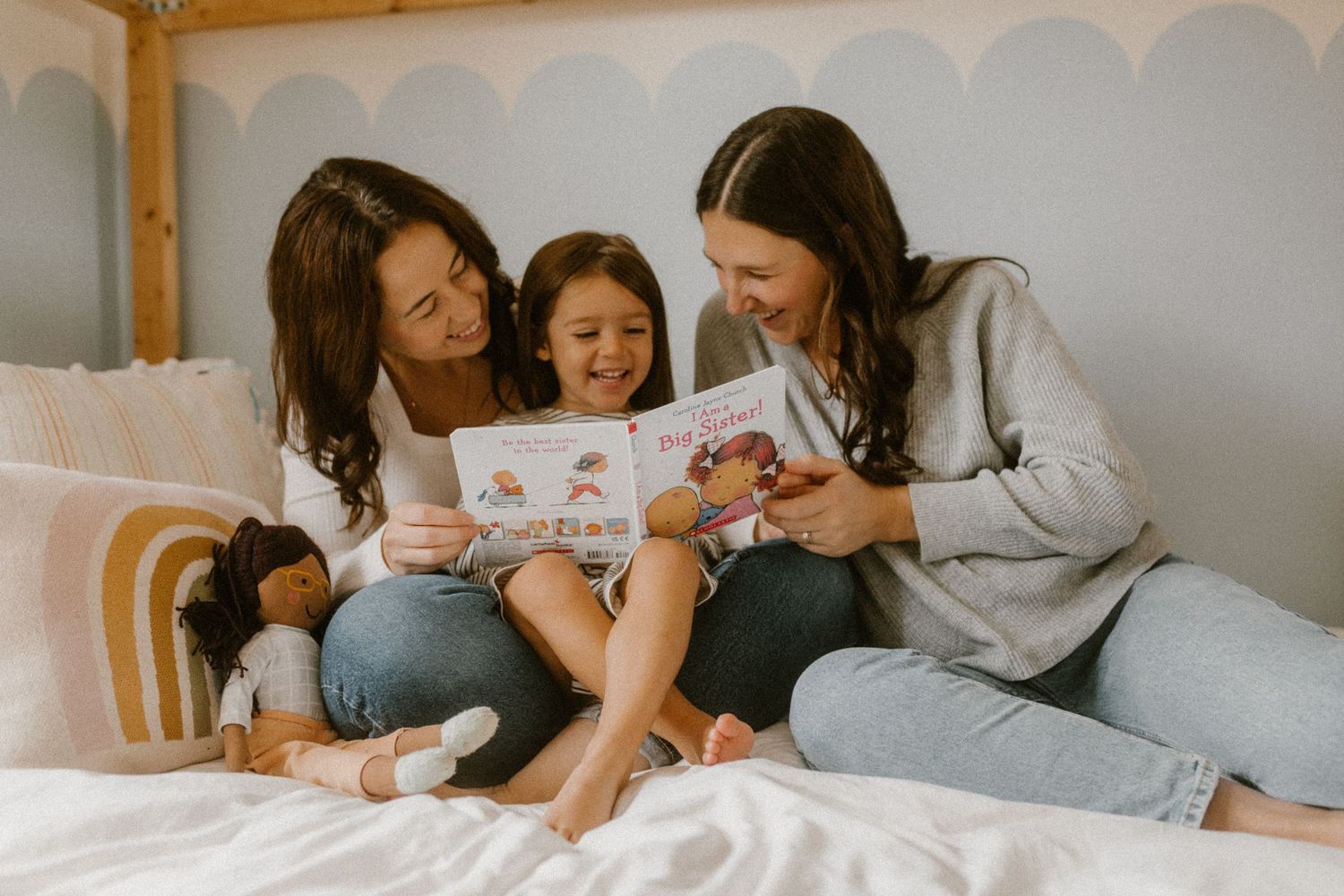 Three people reading a book together on a bed with decorative pillows.