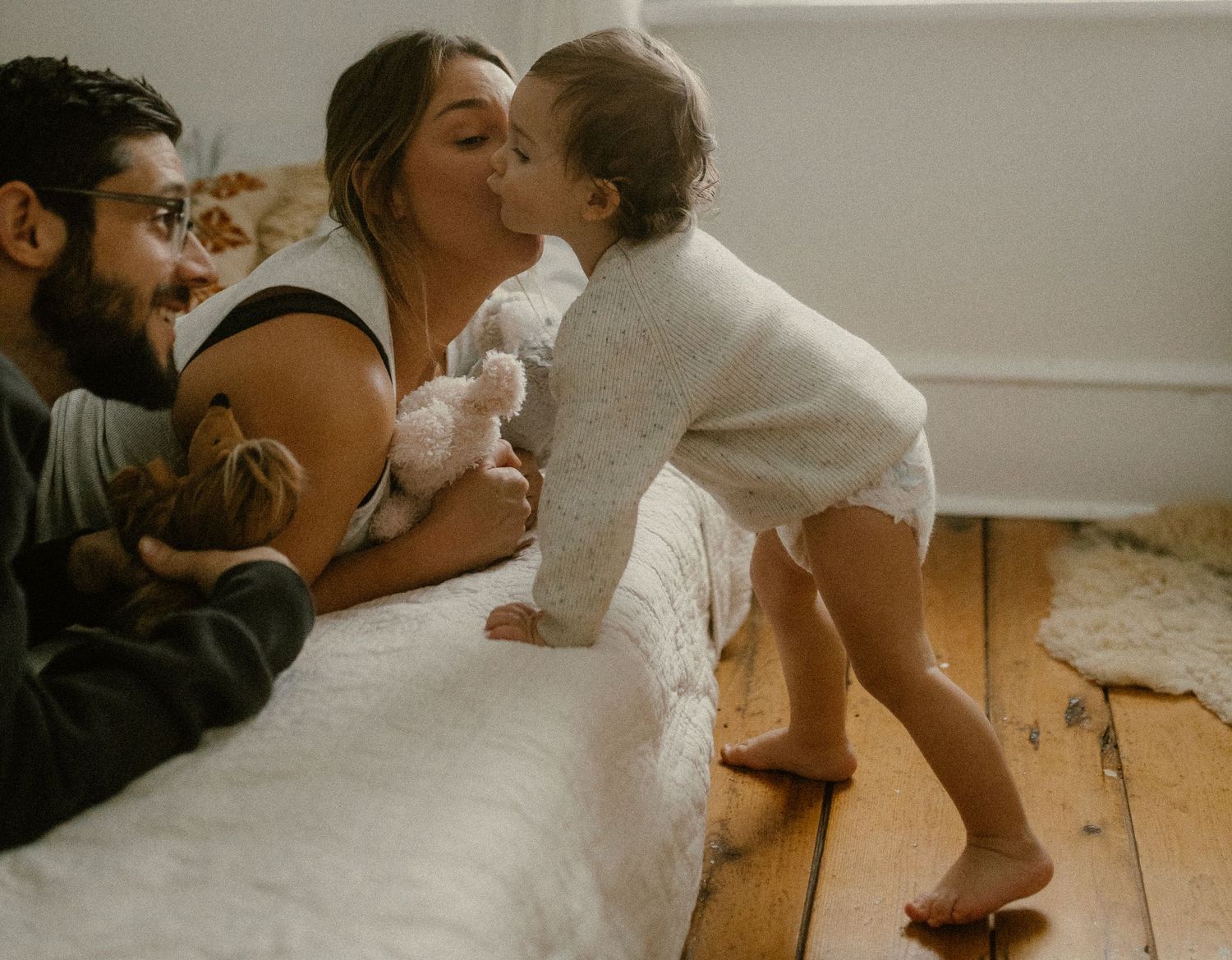 Intimate family moment captured on wooden floors with soft natural lighting and gentle expressions.