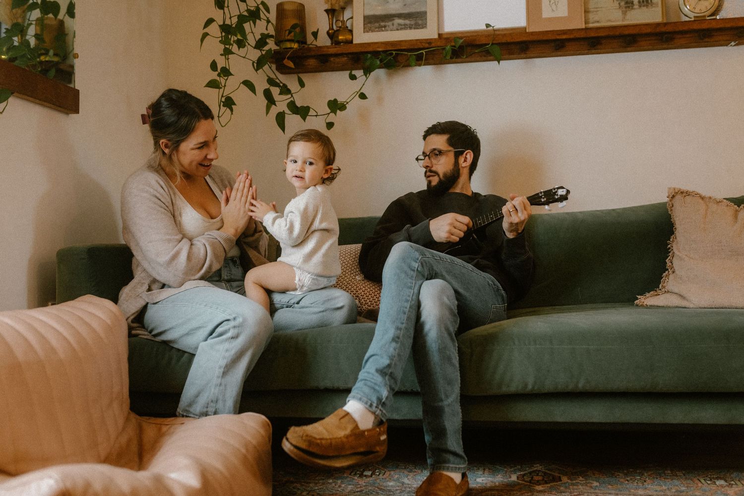 Family gathering on green couch in living room decorated with hanging plants and wooden shelves.