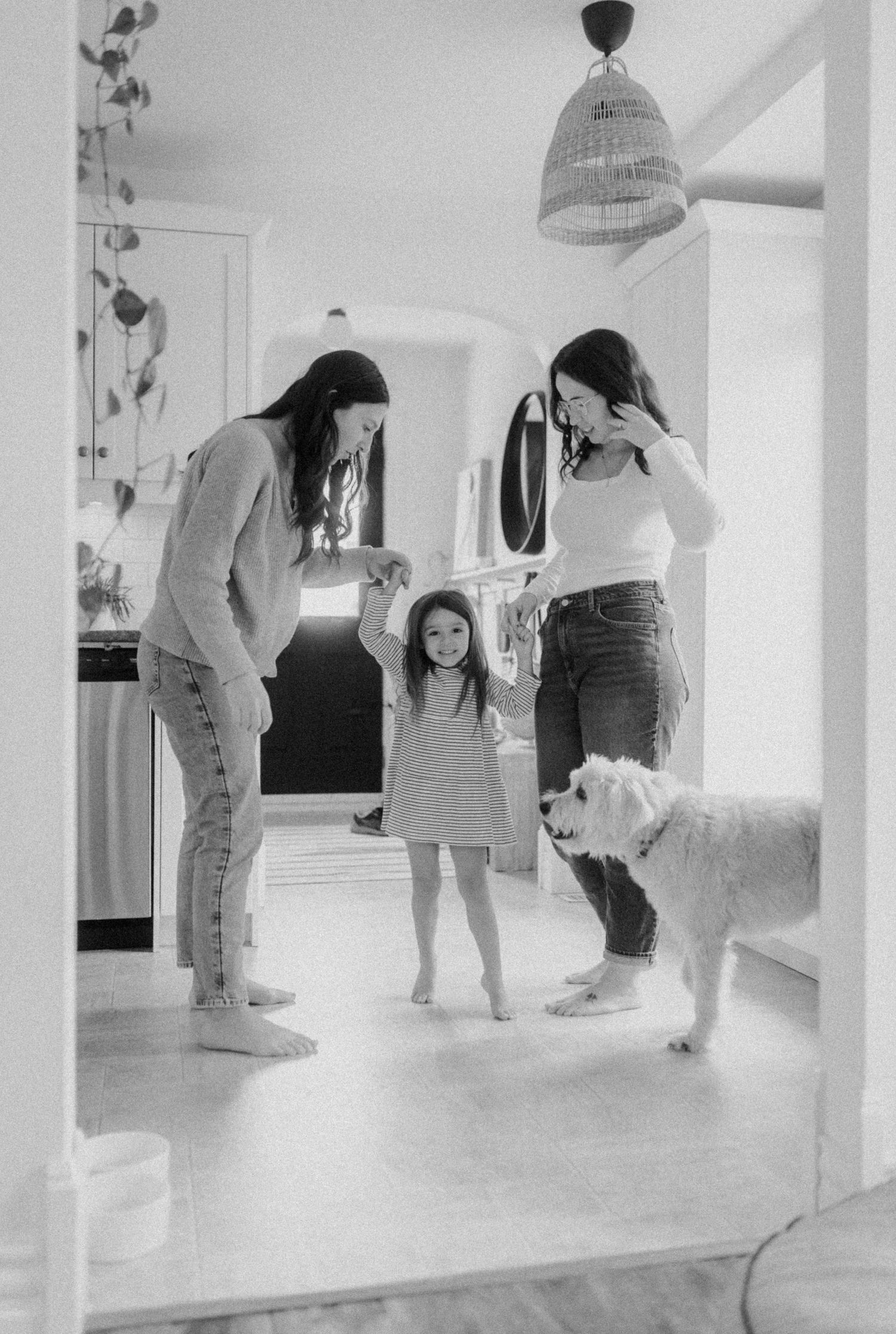 Black and white photo of a playful scene in a bright home kitchen with a friendly white dog.