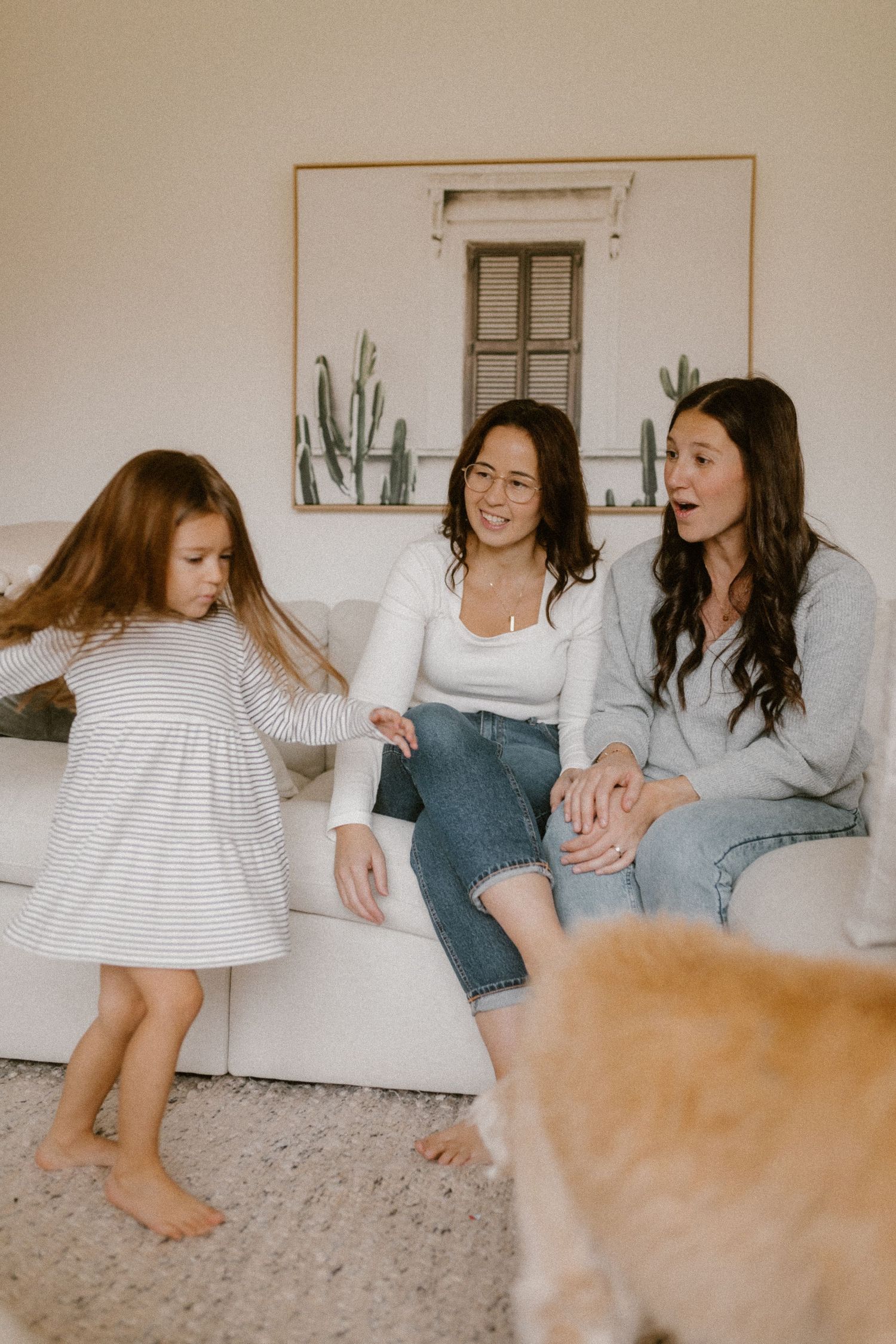 Three people share a joyful moment on a couch while a golden dog appears in the foreground.