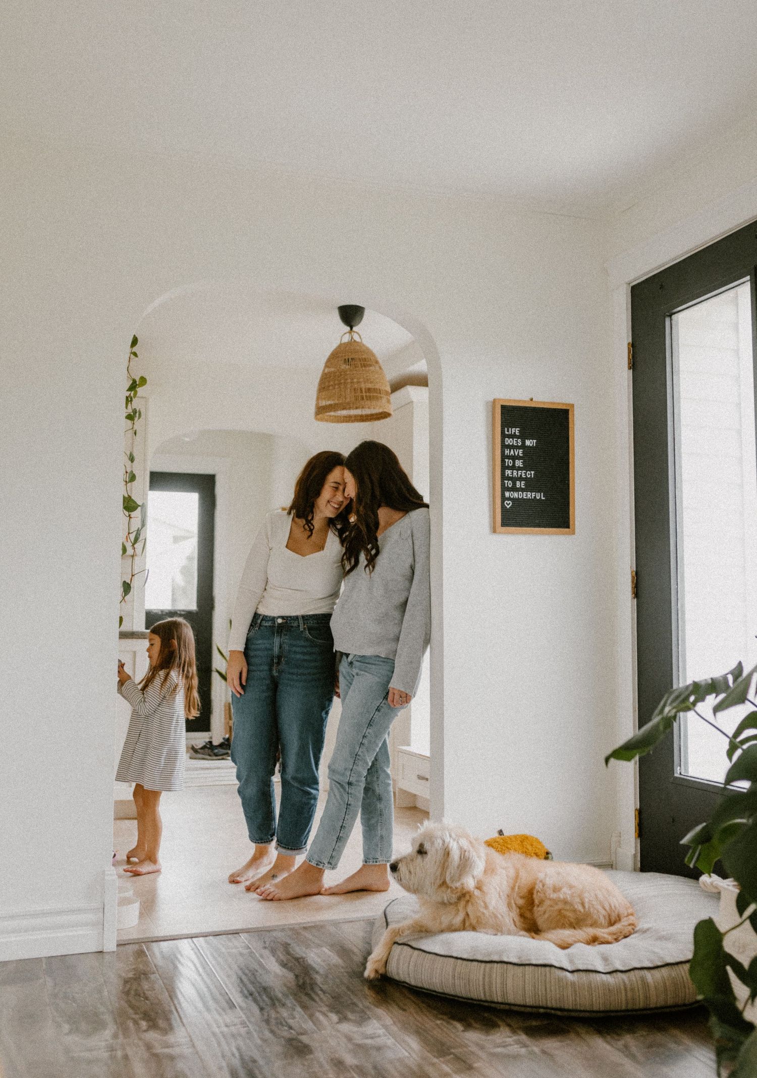 A casual family scene with two moms and dog lounging while others interact in a bright hallway.