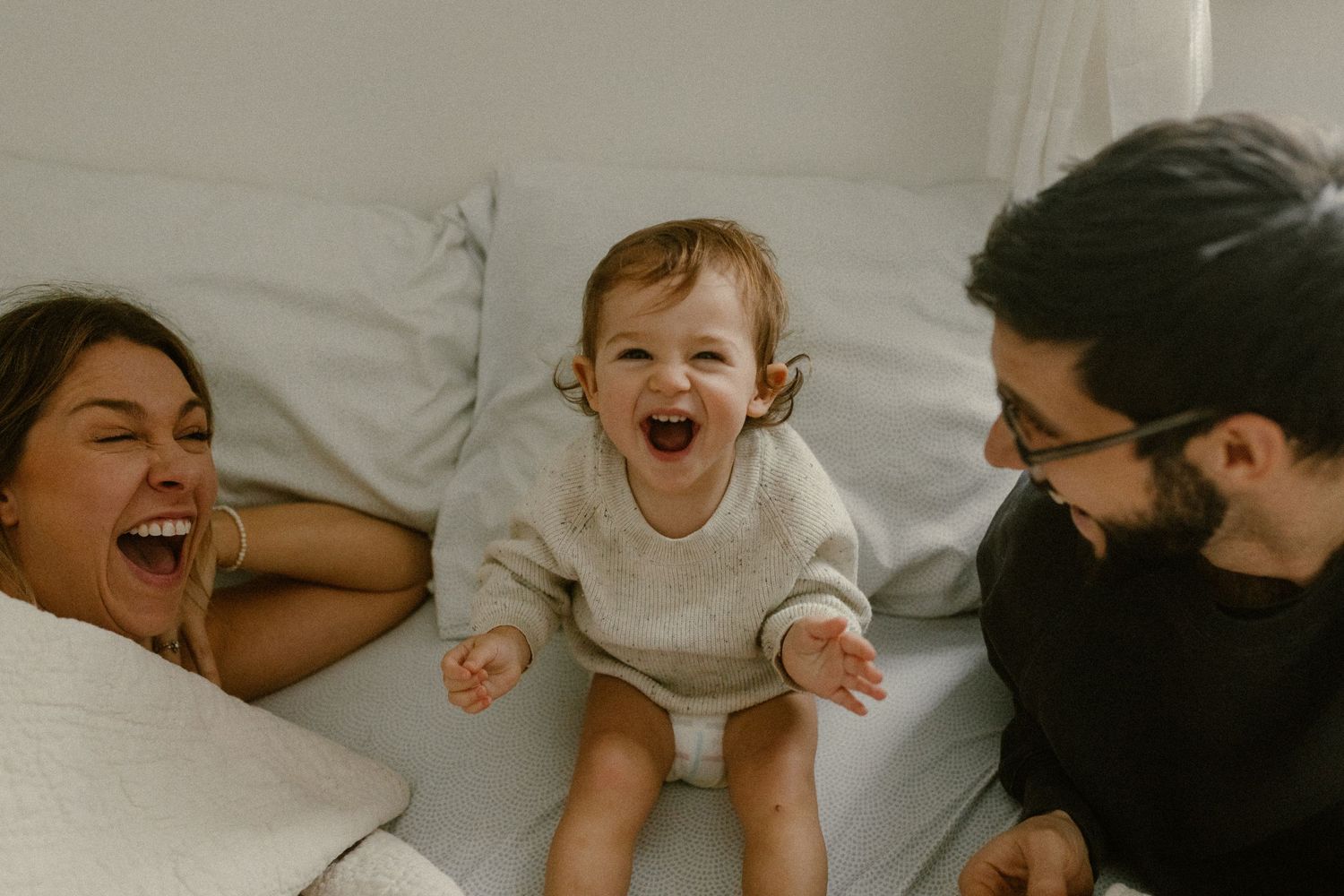 Spontaneous moment of shared laughter and joy captured in warm tones on white bedding.