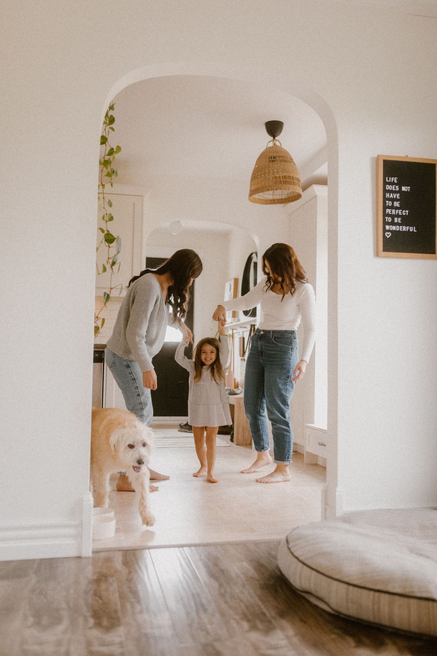Modern white home interior with an arched doorway featuring queer family and dog.