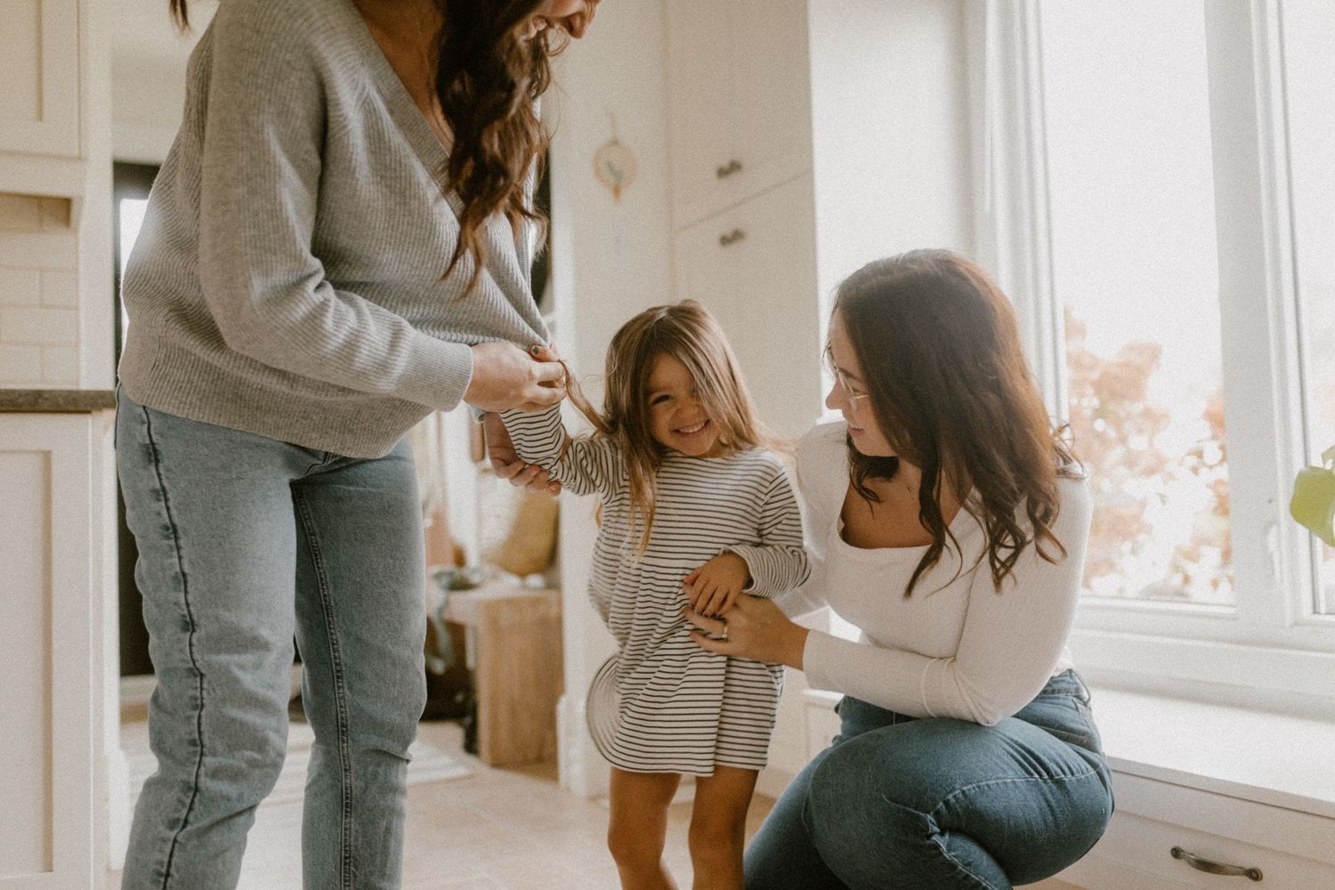 Three people sharing a tender moment together in bright white kitchen setting.