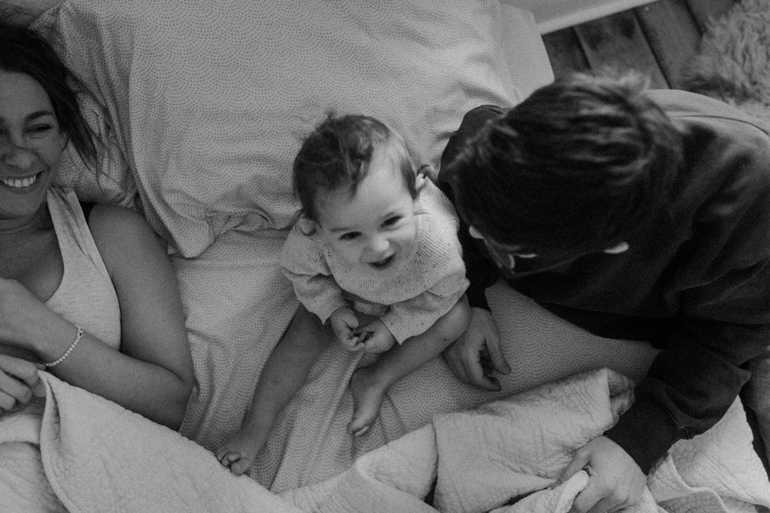 A black and white candid photo of a family sharing a joyful moment together on a bed.