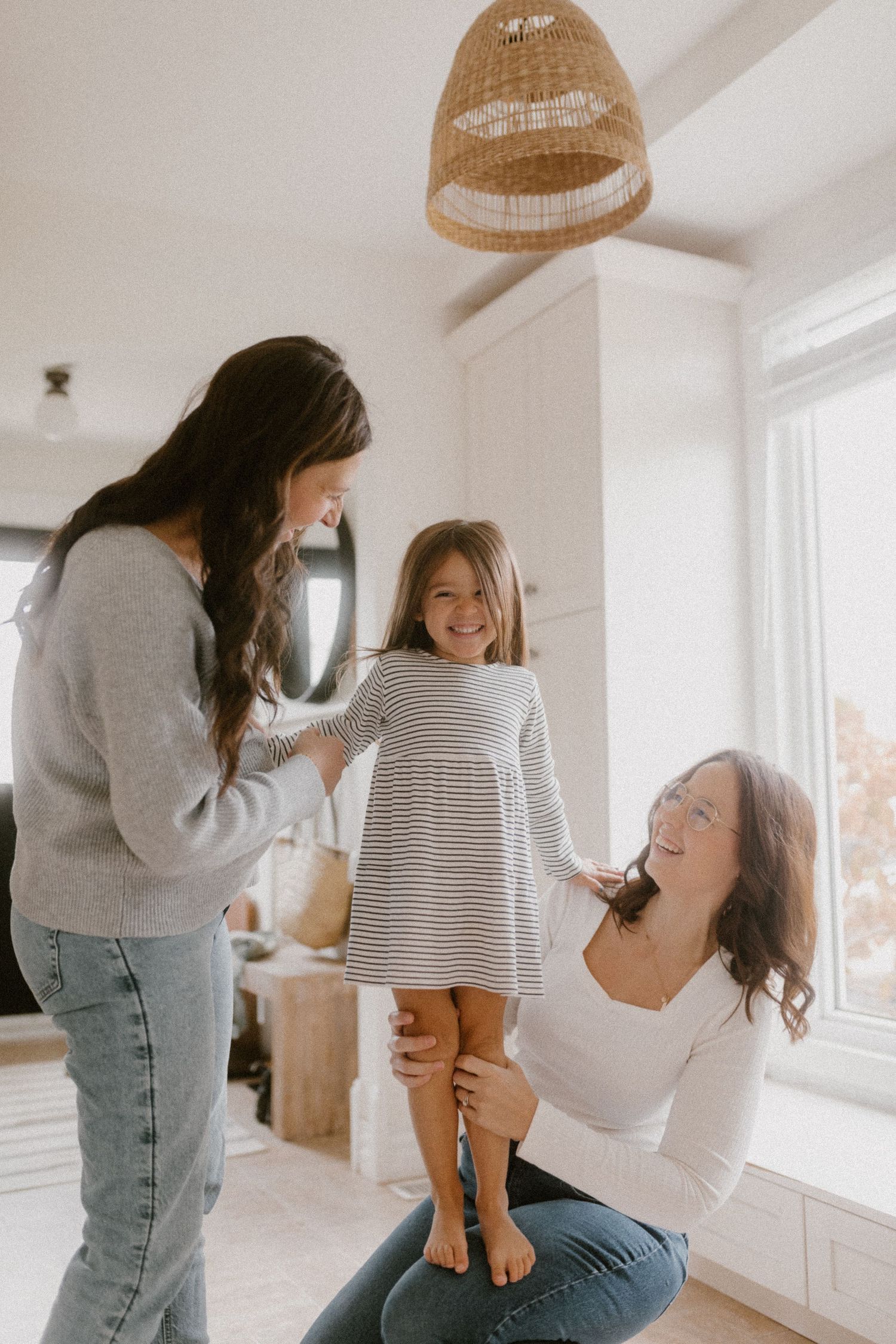 A queer family share a joyful moment together in a bright, modern living room with natural lighting.