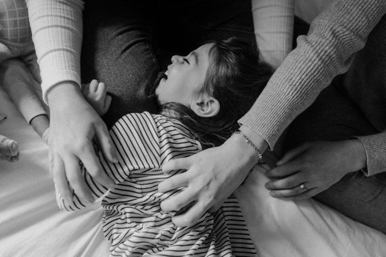 Intimate black and white photo capturing hands tickling their daughter and expressions of joy on a light background.
