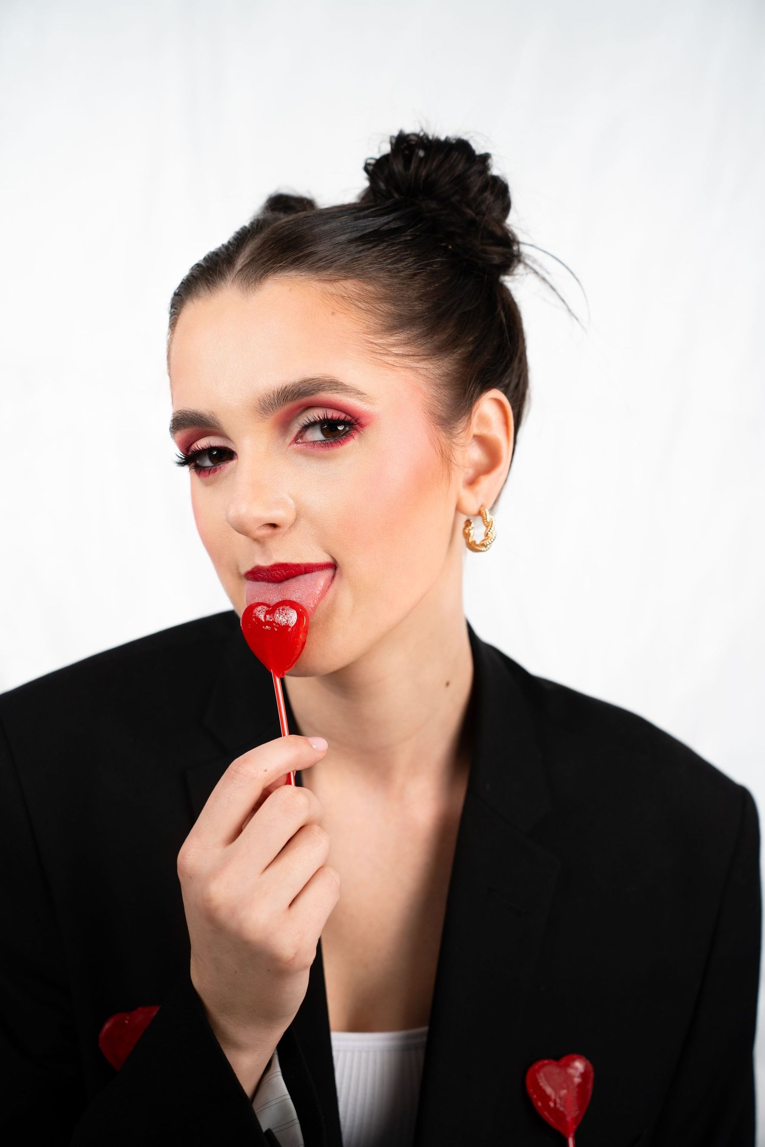 Portrait of model with dark hair holding heart-shaped lollipop wearing black blazer.