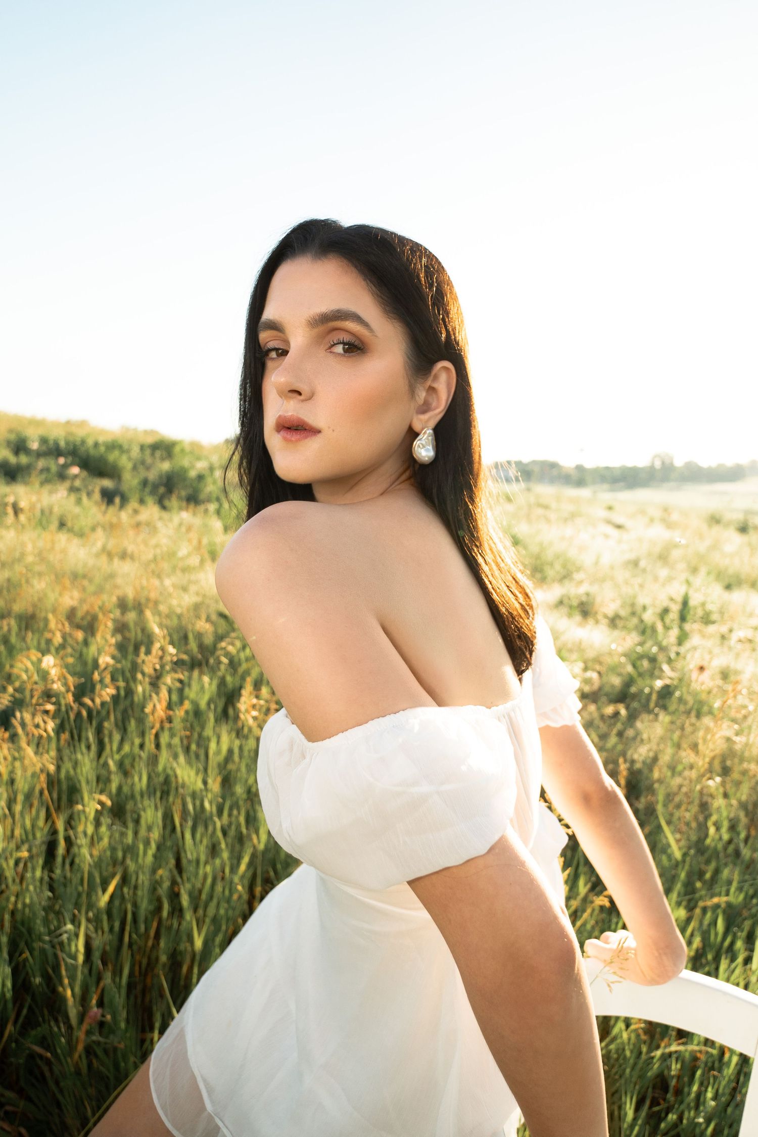 Woman in white off-shoulder dress posing in a golden field at sunset.