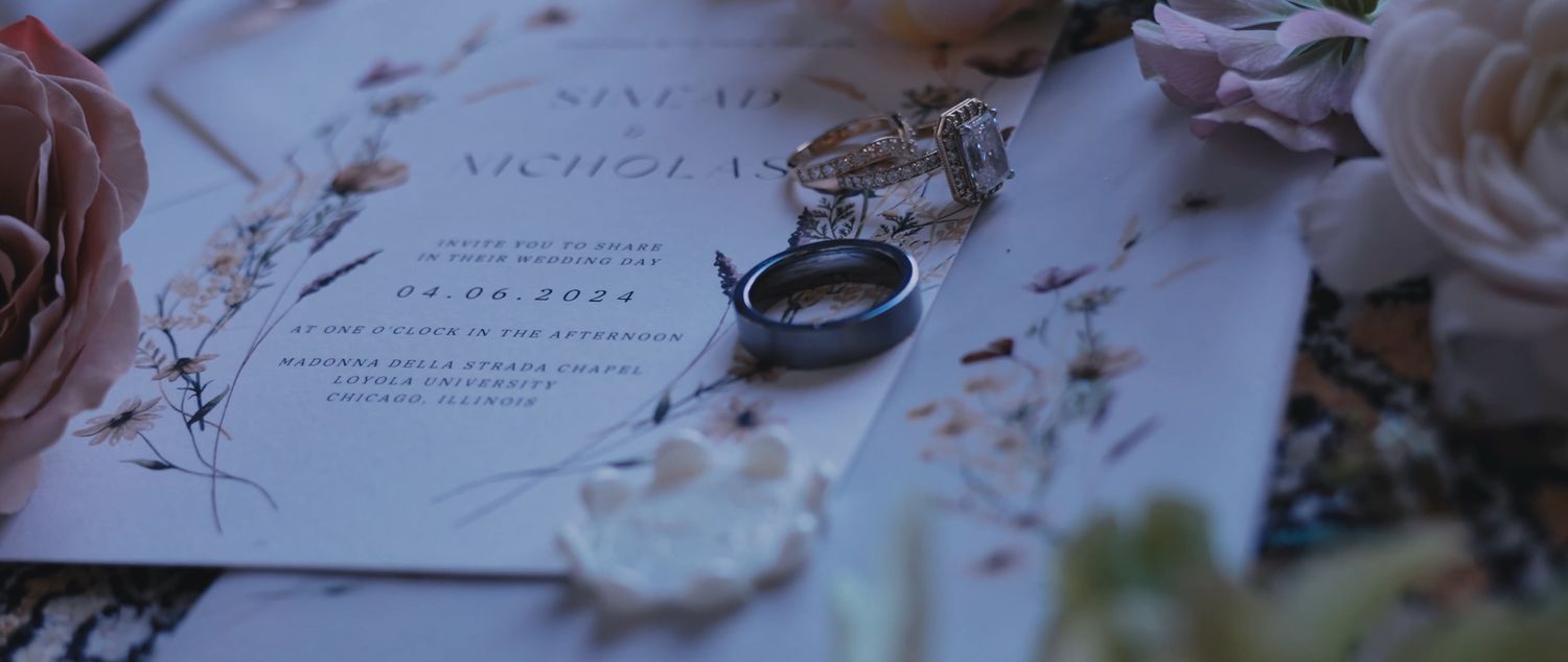 Wedding ring and invitation displayed with delicate pink flowers and petals in a romantic arrangement.
