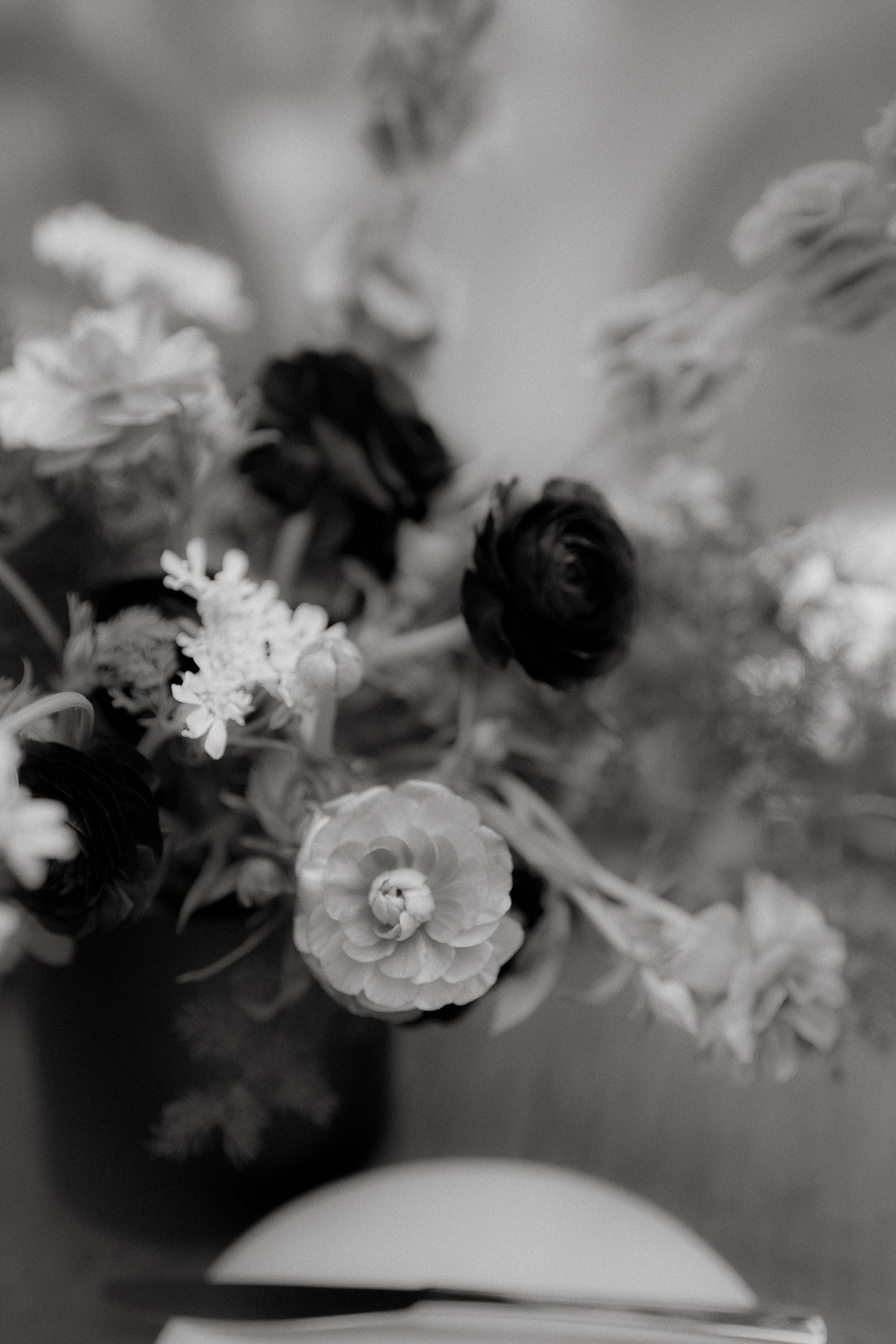 Black and white photograph of delicate flowers in a vase with soft focus creating a dreamy, romantic atmosphere.