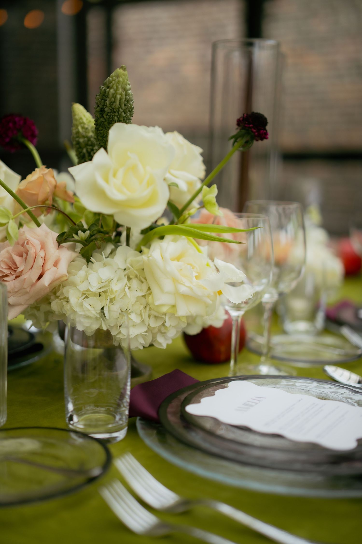 Close-up of white and pink floral centerpiece on elegant table setting with green tablecloth.