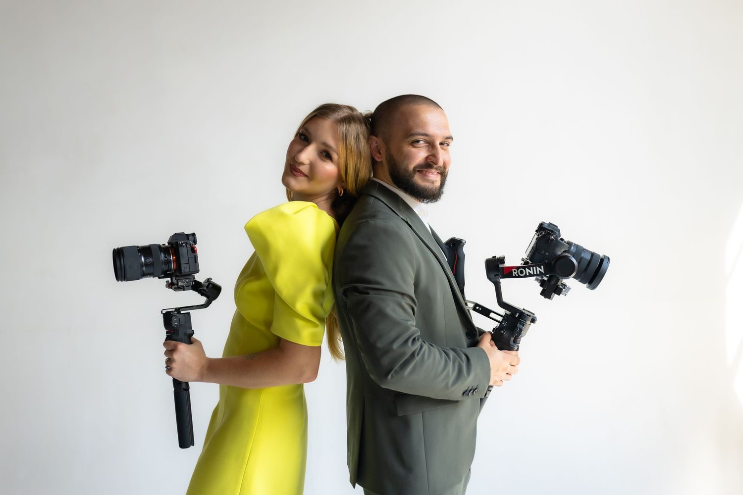Professional photographers posing back to back with camera gimbals against white background.