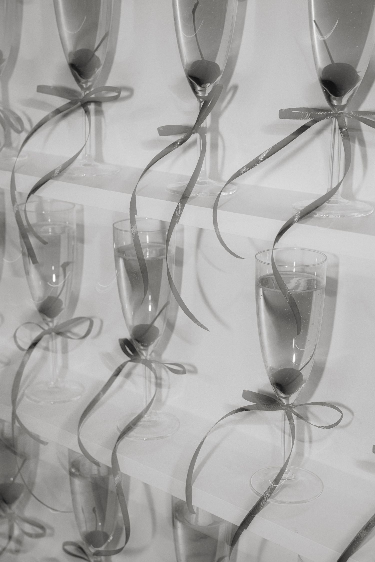 Elegant champagne flutes decorated with gray ribbons arranged in rows creating a delicate pattern in black and white.
