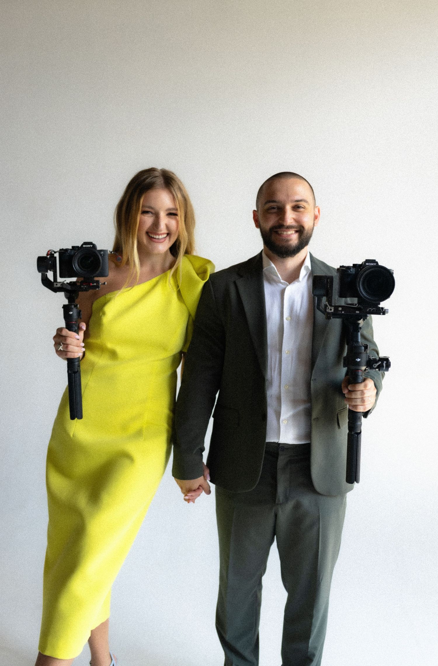 Photography duo in contrasting yellow dress and grey suit holding professional camera equipment.