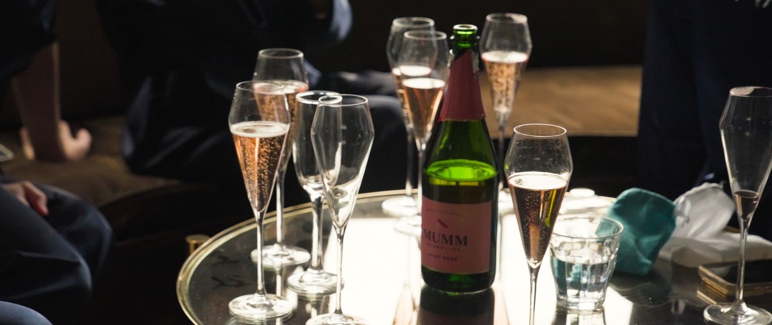 Elegant champagne flutes and a green bottle of sparkling wine arranged on a golden tray at a sophisticated event.