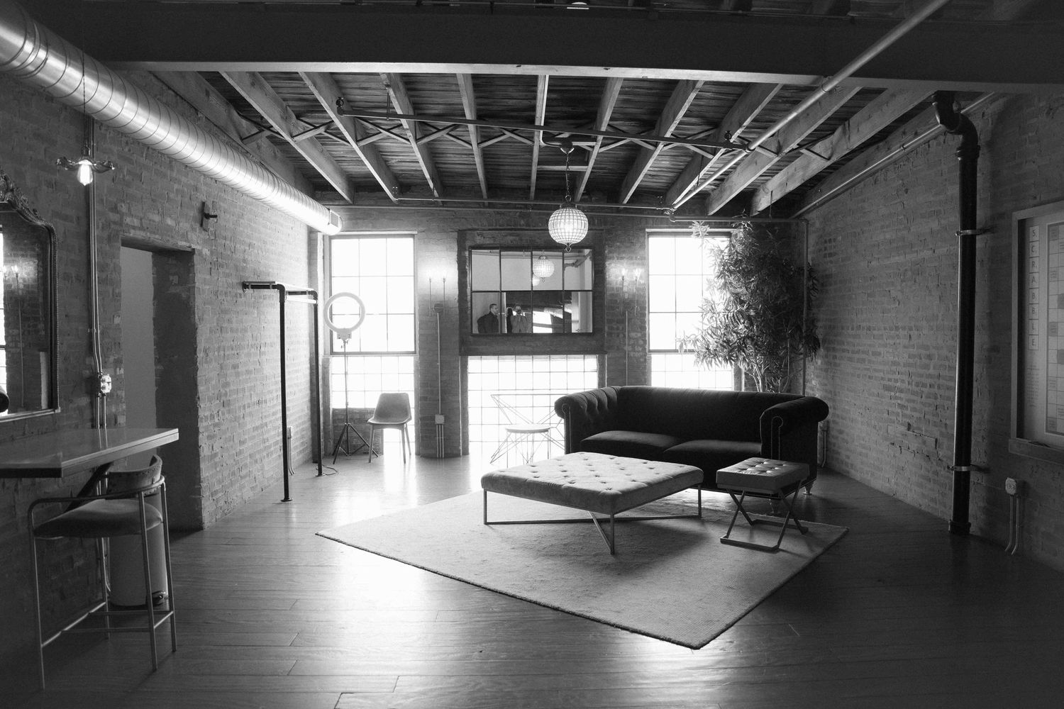 Modern industrial office space with exposed brick walls features a black sofa and hardwood floors. By FORGET ME NOT ARTS
