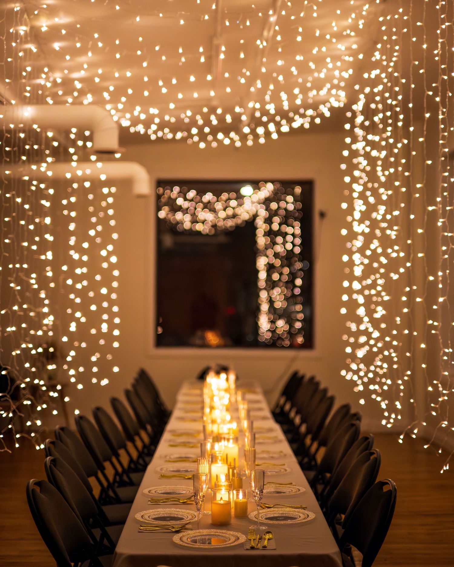 A long dining table set for an elegant dinner under cascading twinkle lights creating a magical atmosphere.