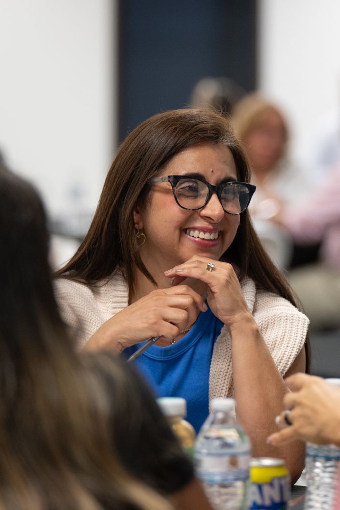 Person in glasses and white sweater smiling and laughing during a meeting with water bottles on the table.