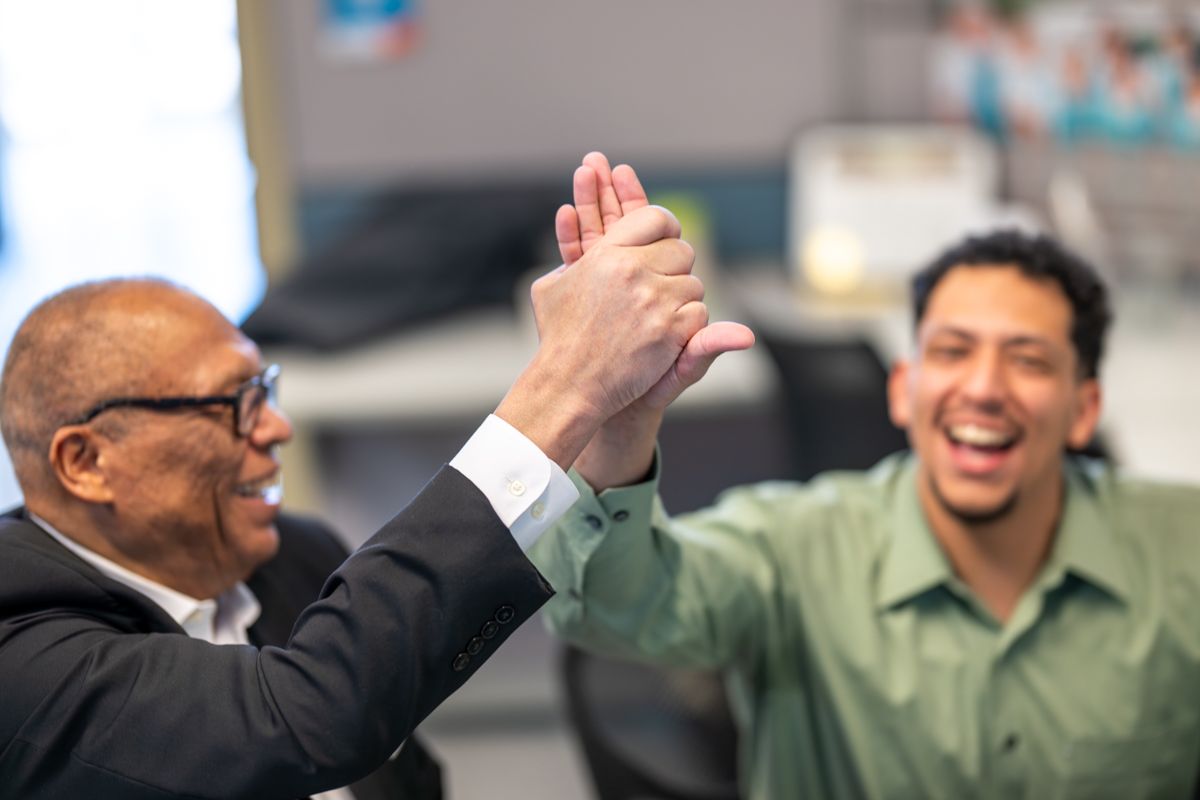 A group of diverse business professionals laughing and celebrating together in an office setting.