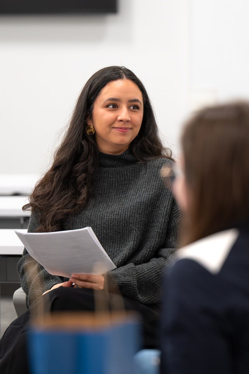A woman in a black sweater reads documents during what appears to be a business meeting.