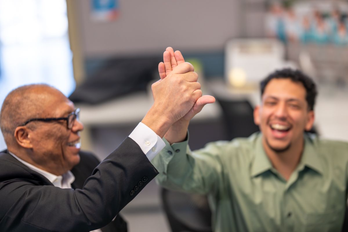 Two men sharing a high five and laughing together in an office setting, celebrating success.