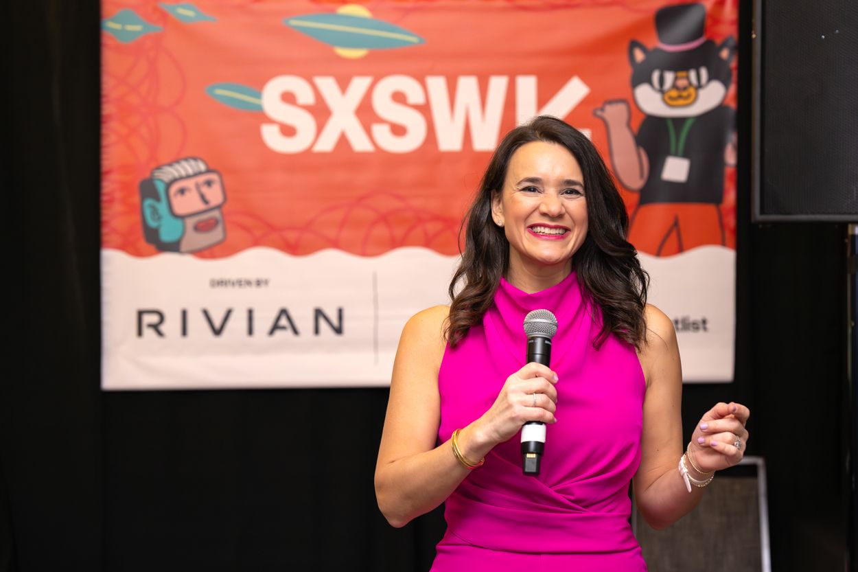 Woman in pink dress speaks on stage at SXSW event sponsored by Rivian, holding microphone.