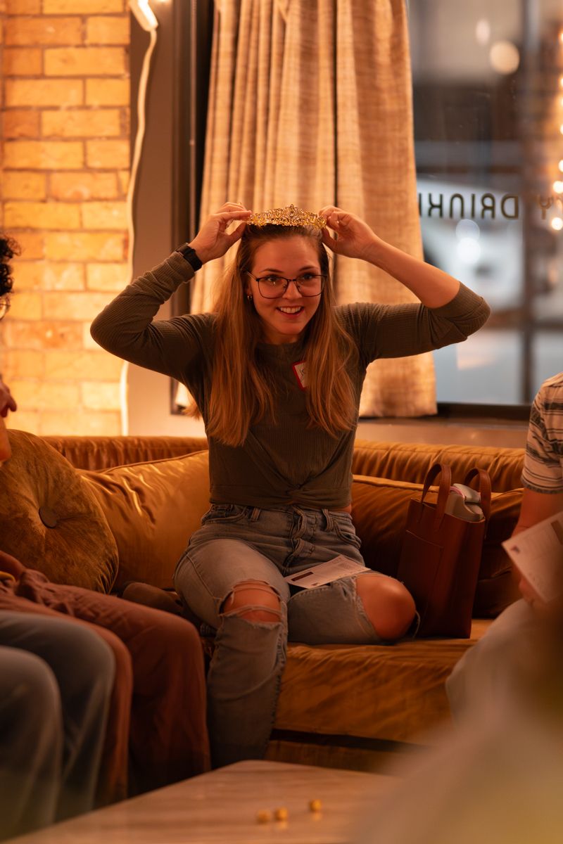 Person relaxes on brown leather couch in warm-lit room with exposed brick walls.