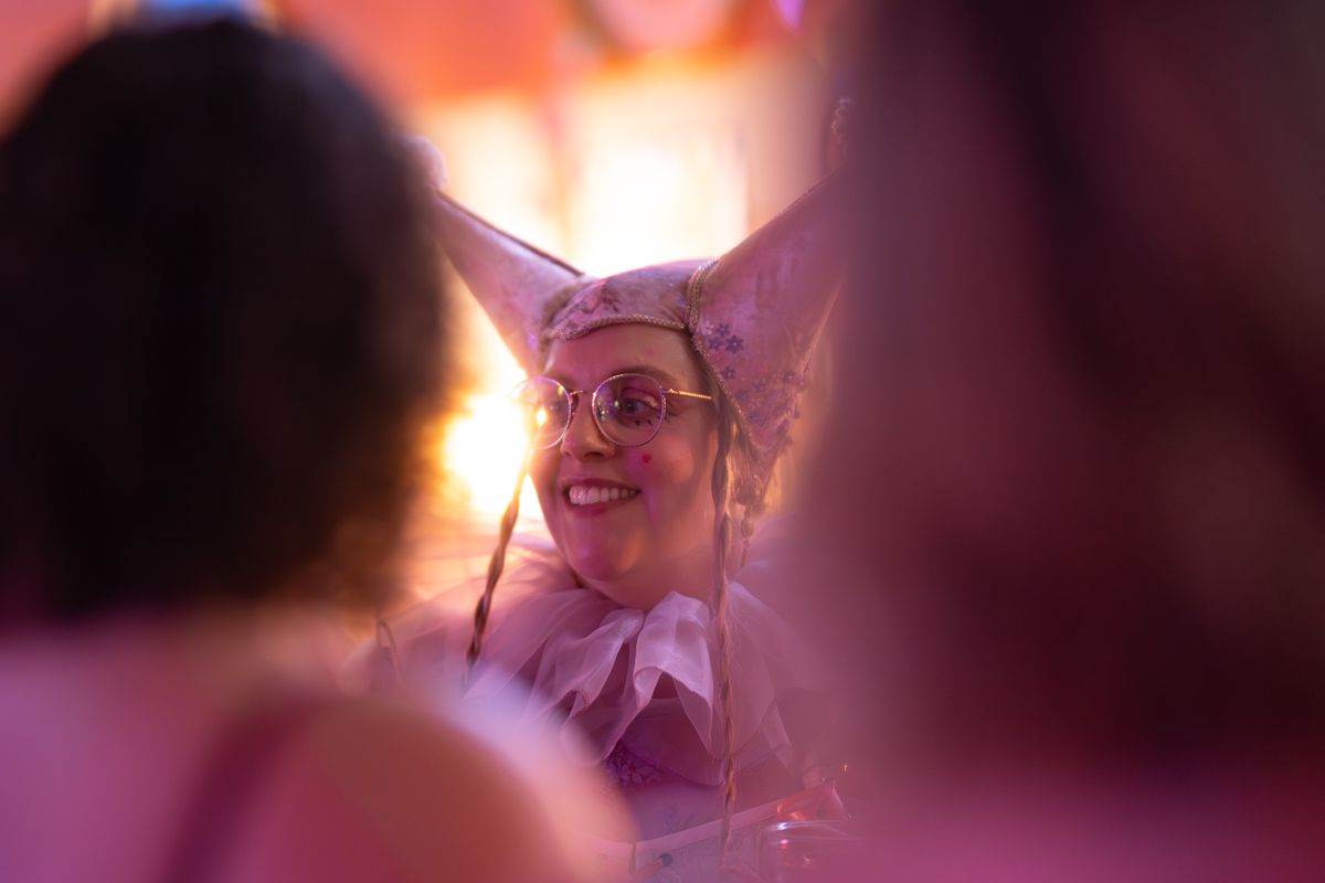 Woman in pink bunny costume and glasses smiling at a festive party event with warm pink lighting.