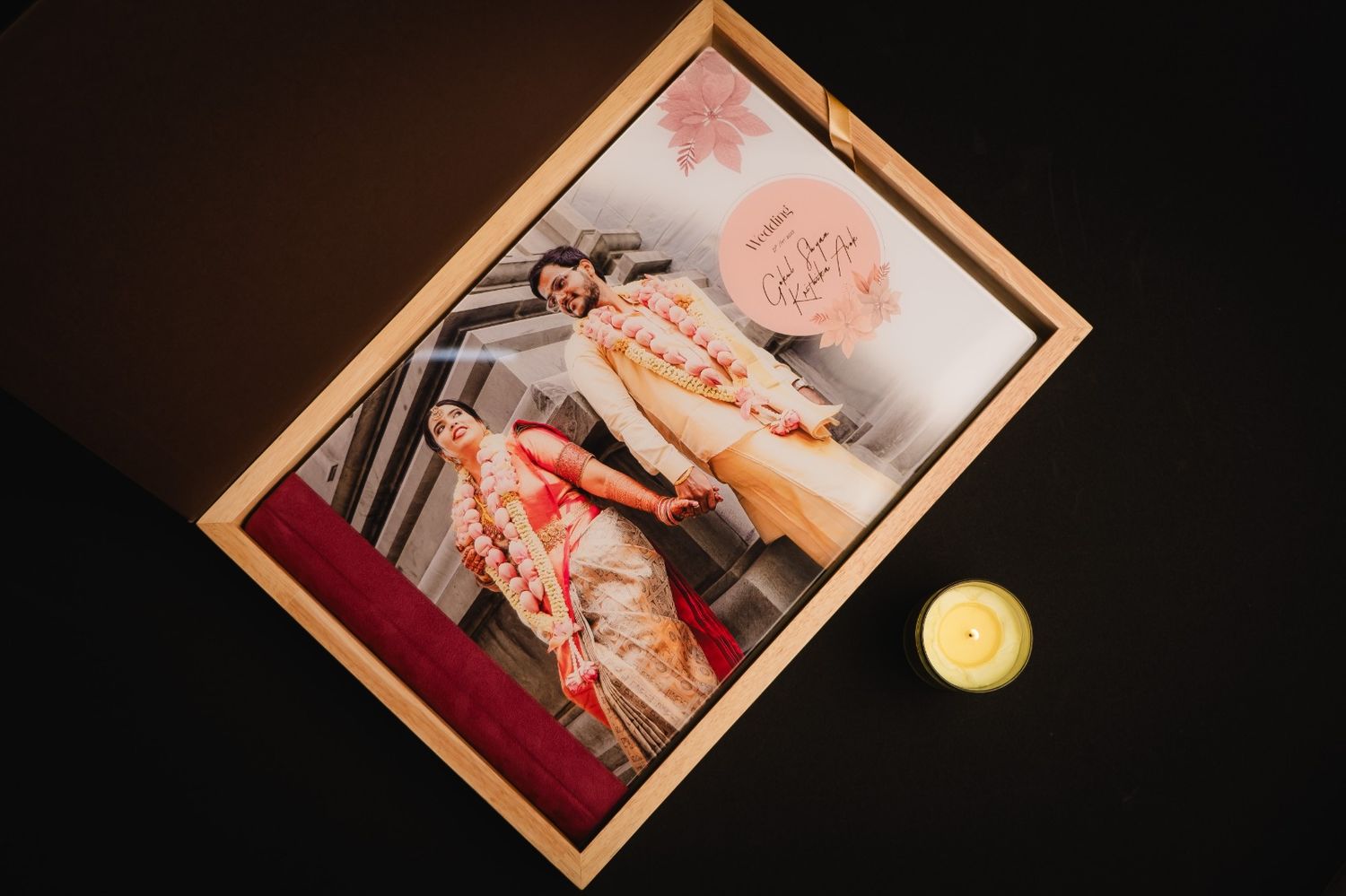 Framed photo of two women in colorful traditional attire displayed in a wooden box beside a small candle.
