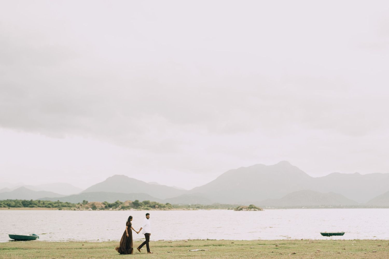 Bride and groom walking along a lakeside landscape with mountains in the background.